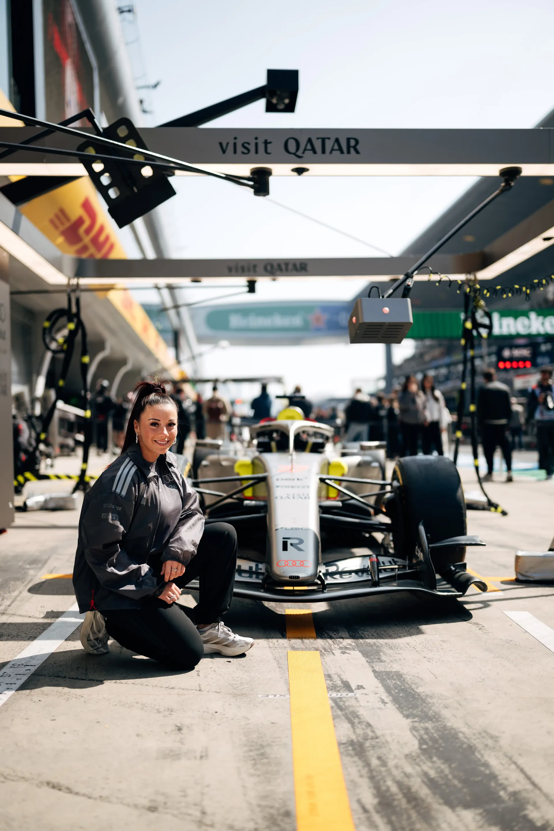 Carrie Schreiner squatting in front of race car, pit lane scene visible behind in China at Shanghai