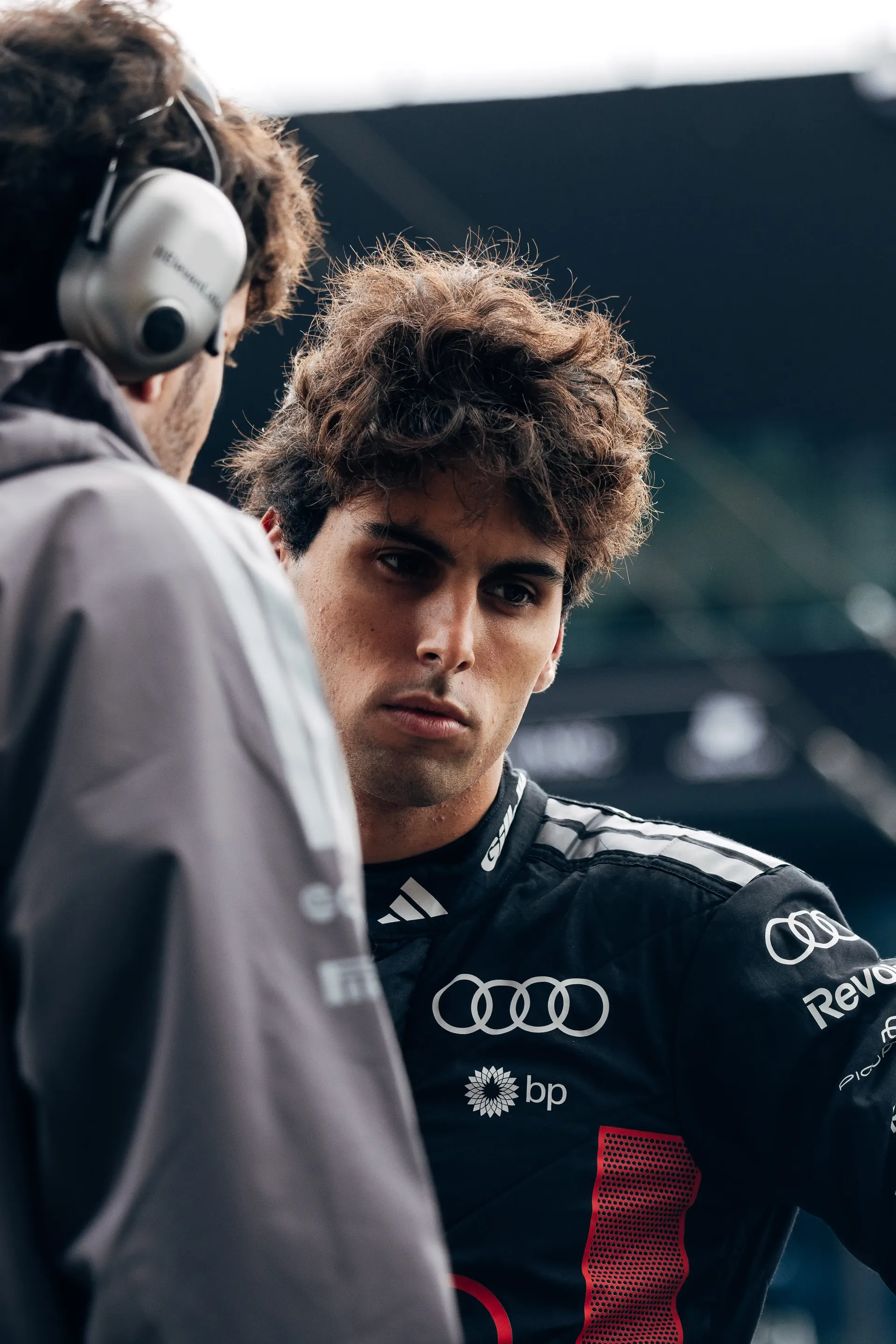 Audi Revolut F1® Team driver Gabriel Bortoleto being interviewed in the paddock at the Dutch Grand Prix, wearing team racewear and headphones visible in the foreground.