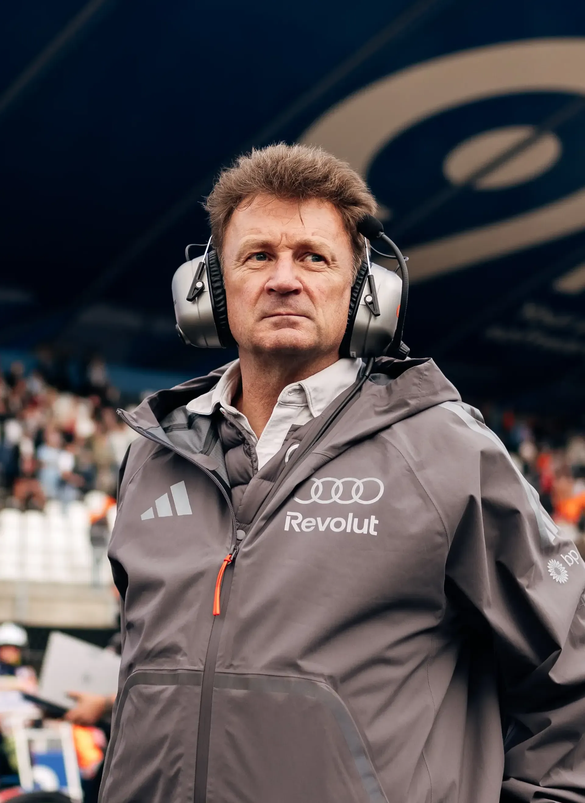 Audi Revolut F1® Team racing director Allan Mcnish standing in the paddock at the Dutch Grand Prix, with the grandstand and crowd in the background.