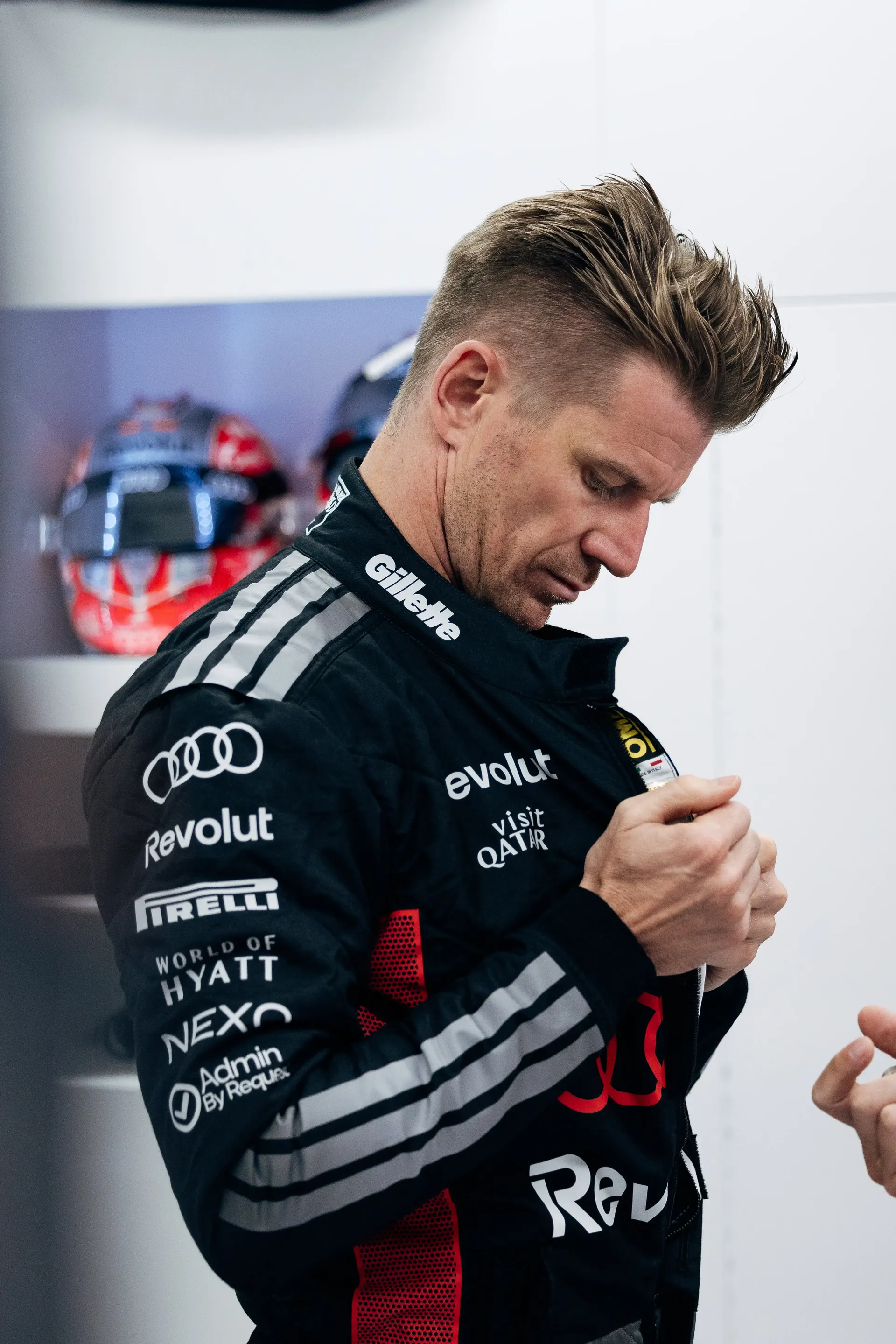 udi Revolut F1® Team driver Nico Hulkenberg adjusting his race suit in the paddock at the Dutch Grand Prix, with an Audi F1 car visible in the background.