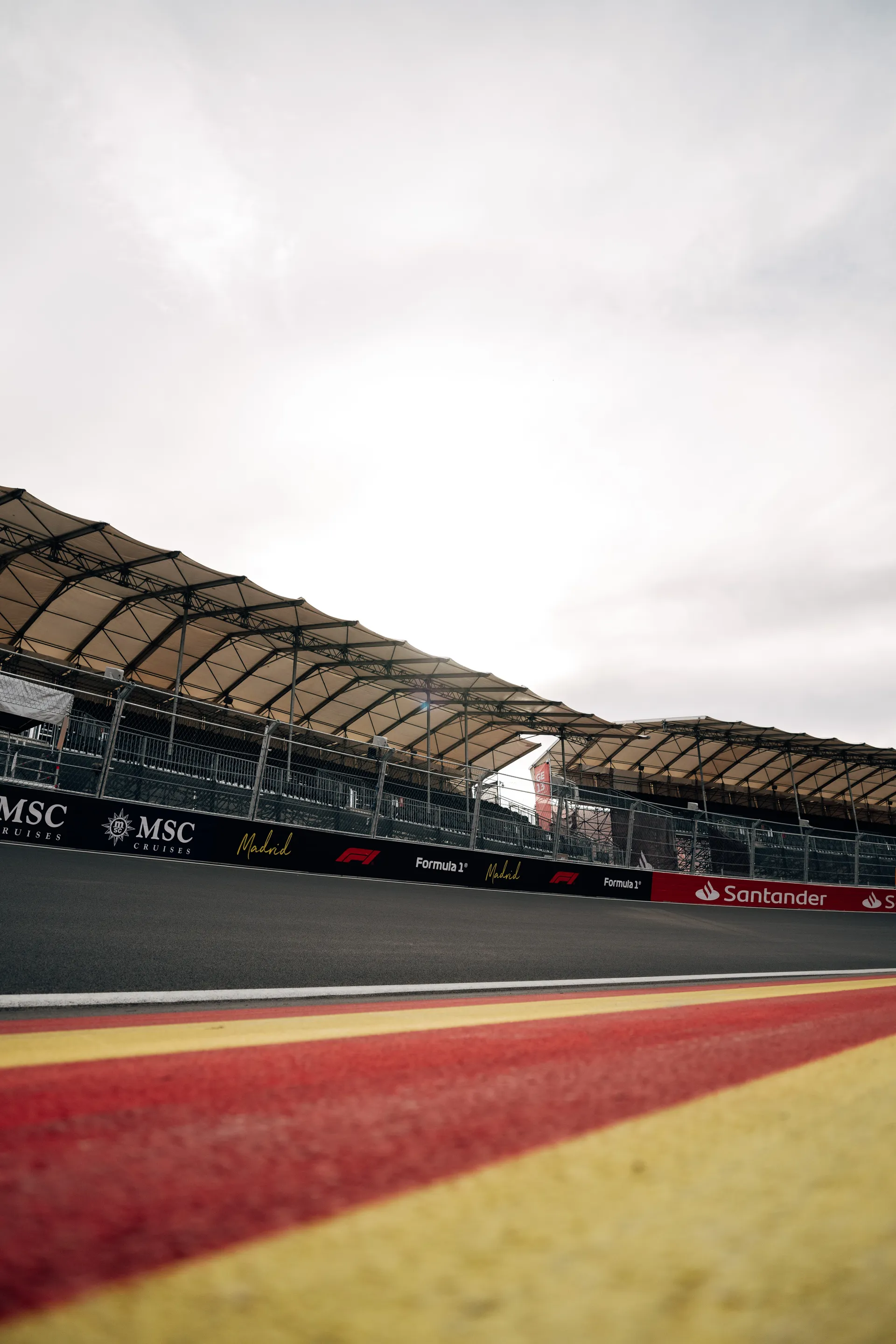 Covered grandstand overlooking the MADRING circuit in Madrid, with red and yellow track markings in the foreground.