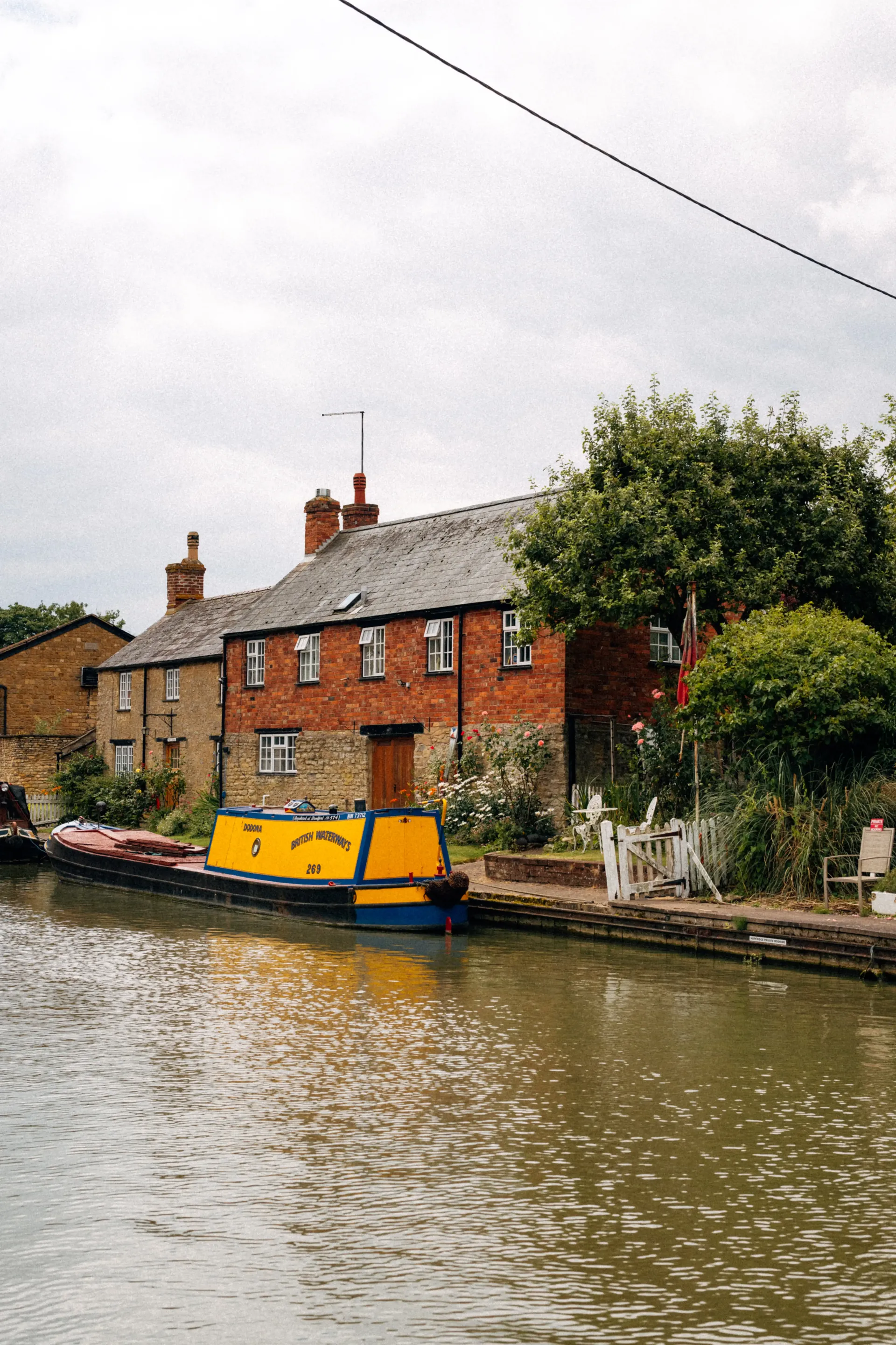 Yellow narrowboat moored along a quiet canal in a village.