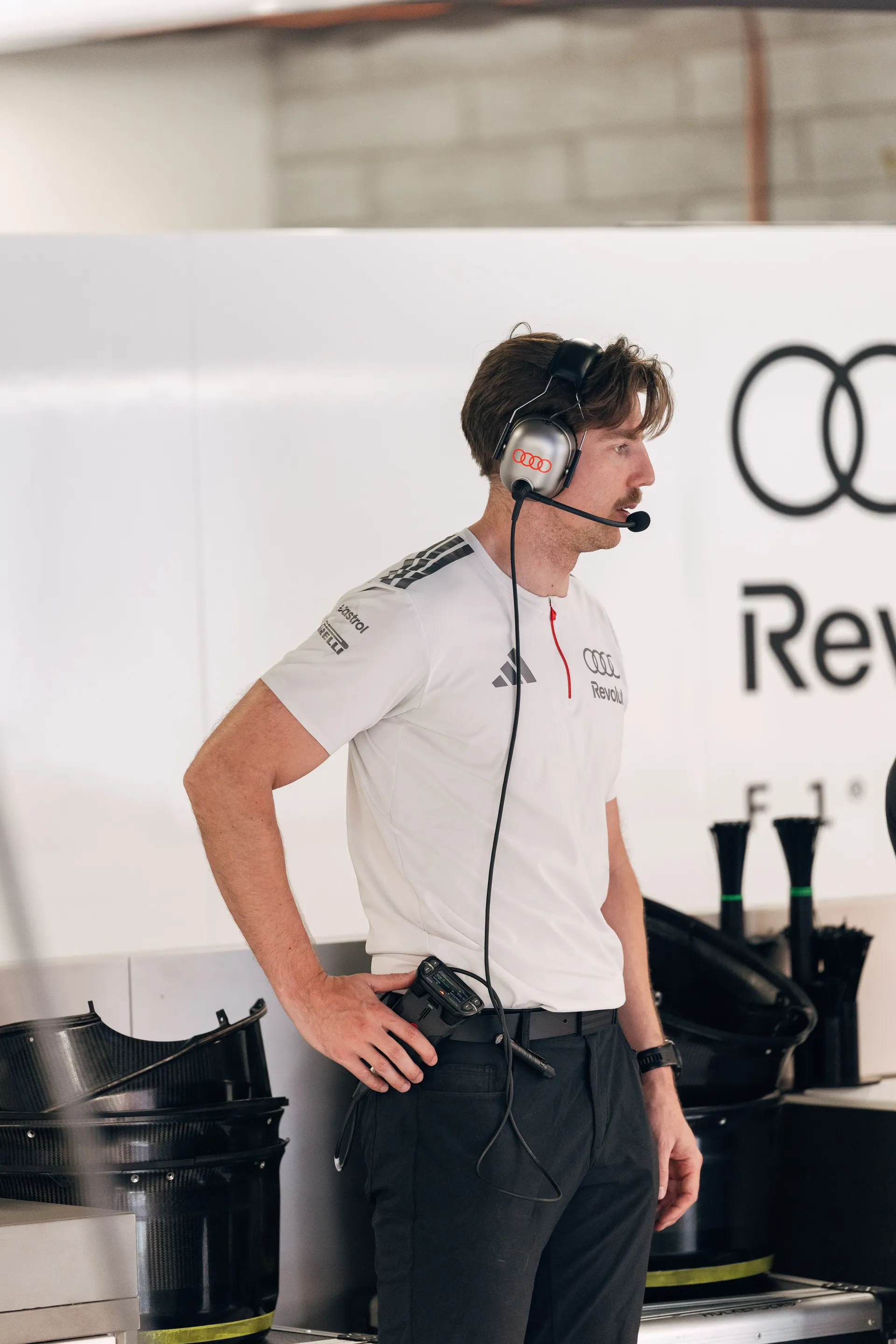 Audi Revolut F1® Team engineer wearing a headset stands beside the Audi R26 in the garage.
