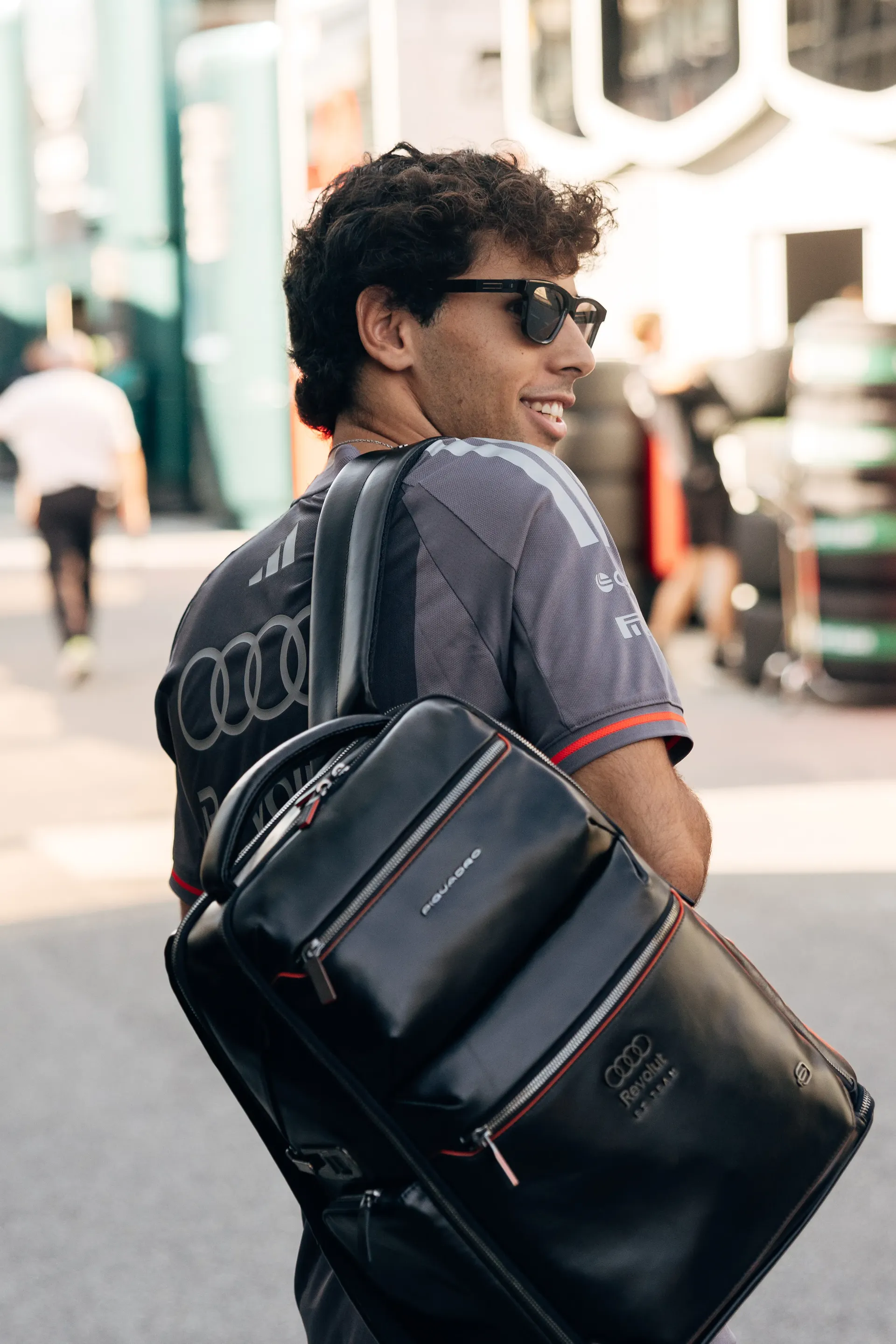 Audi Revolut F1® Team driver Gabriel Bortoleto looks over his shoulder while carrying an Audi-branded team backpack during Thursday arrivals.