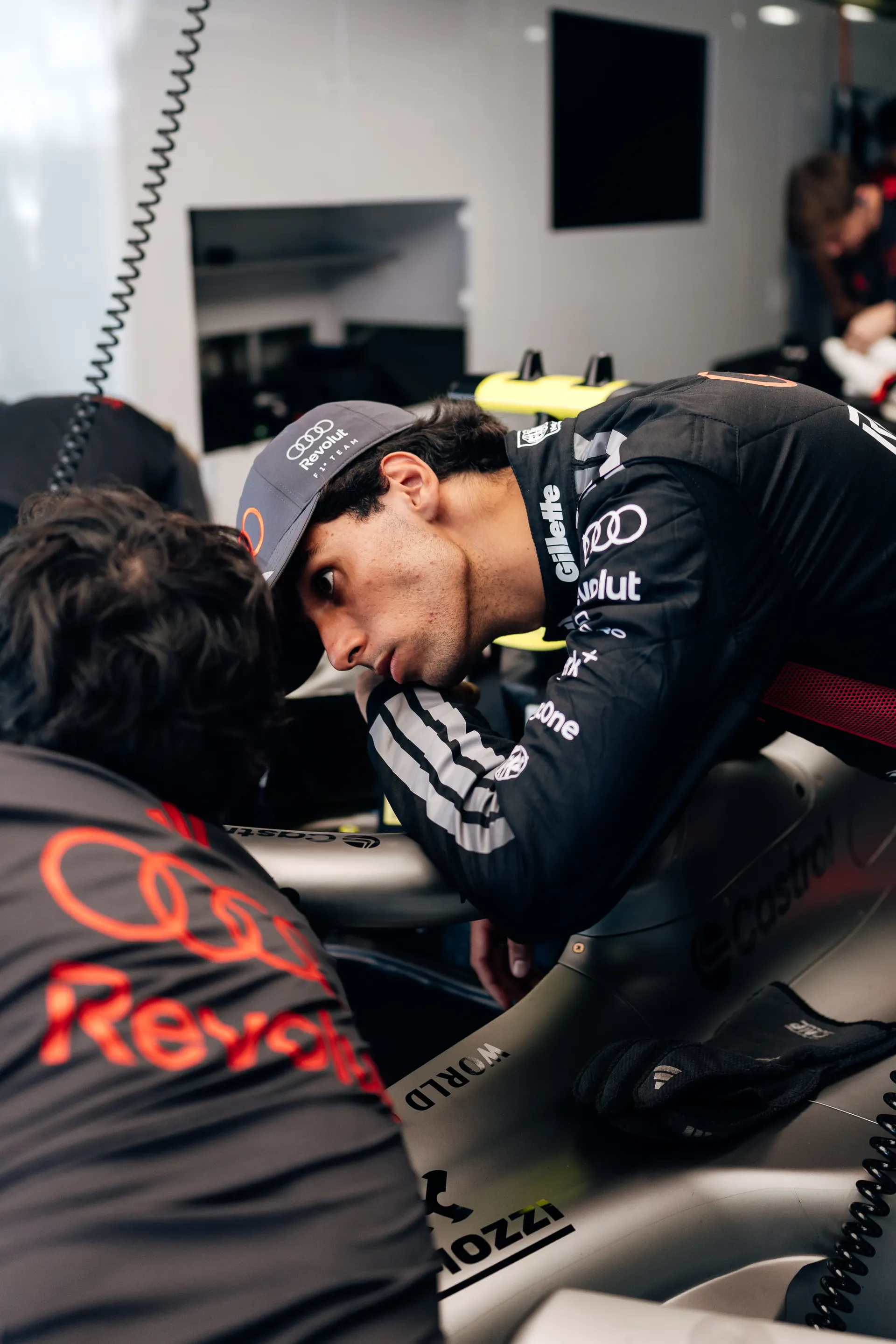 Gabriel Bortoleto leaning over the Audi Revolut F1® Team Formula 1® car inside the garage.