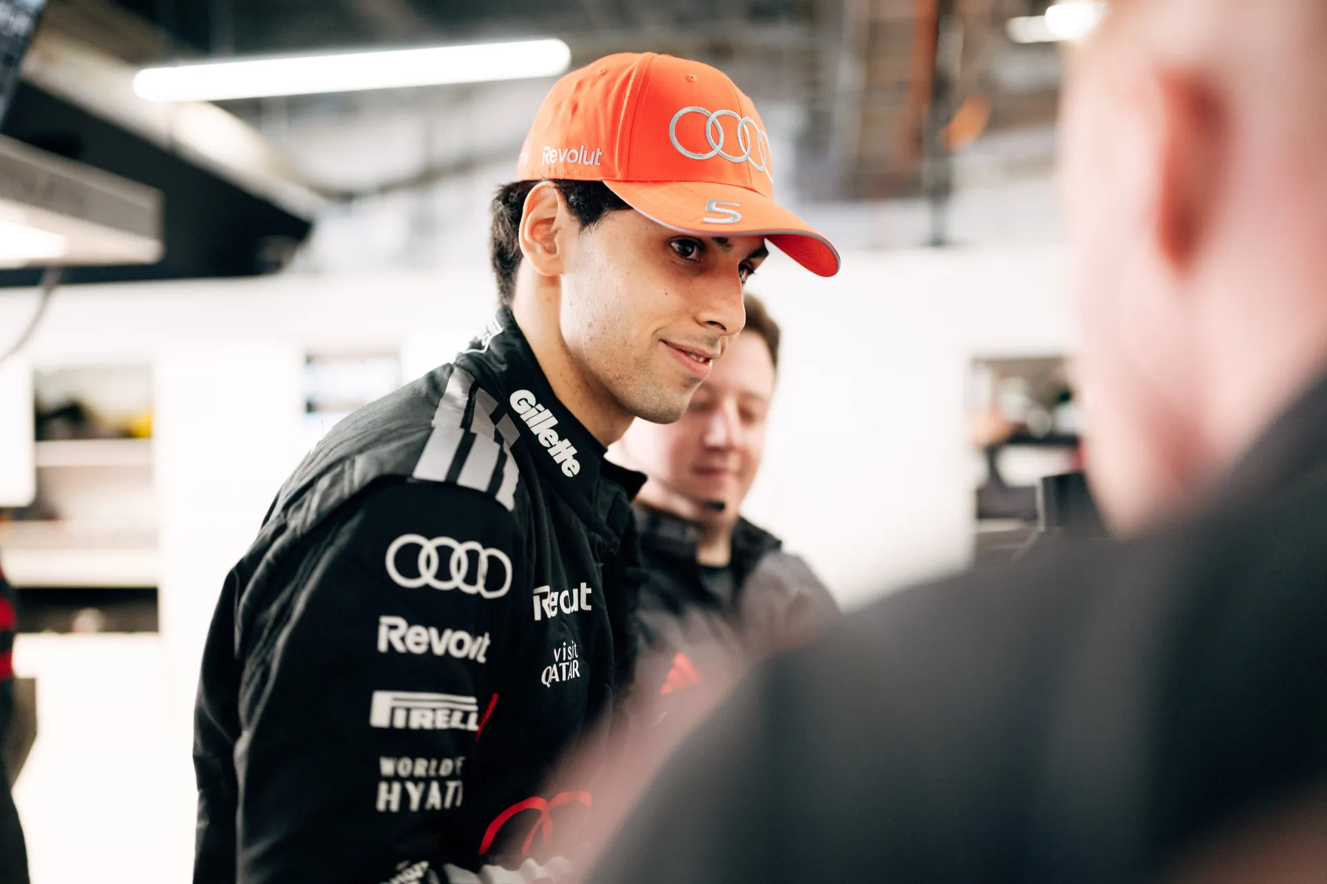 Gabriel Bortoleto in Audi Revolut F1® Team cap and racewear speaking with team members inside the garage before practice.