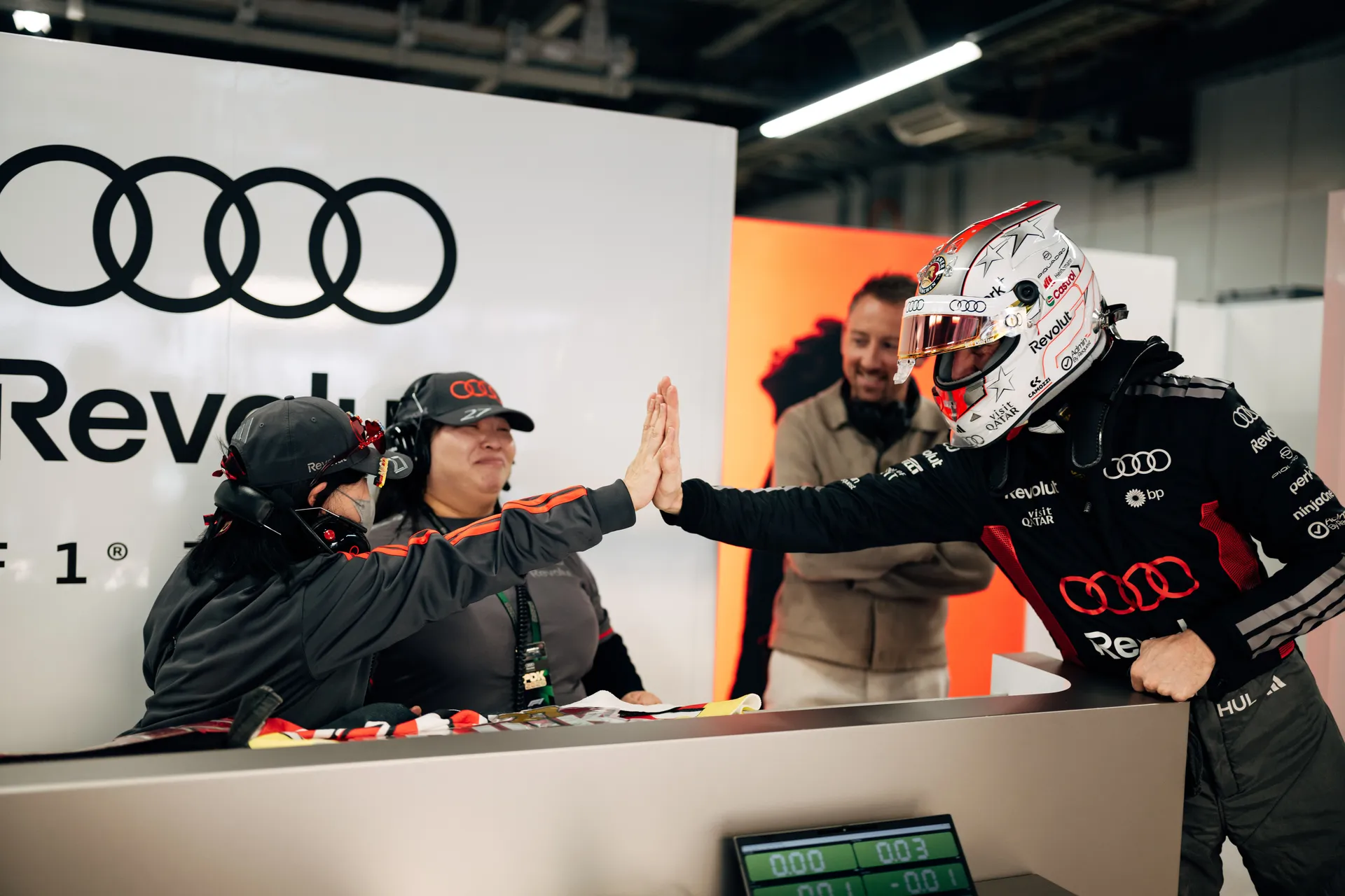 Nico Hulkenberg sharing a high five with a team member at the Audi Revolut F1® Team garage desk.