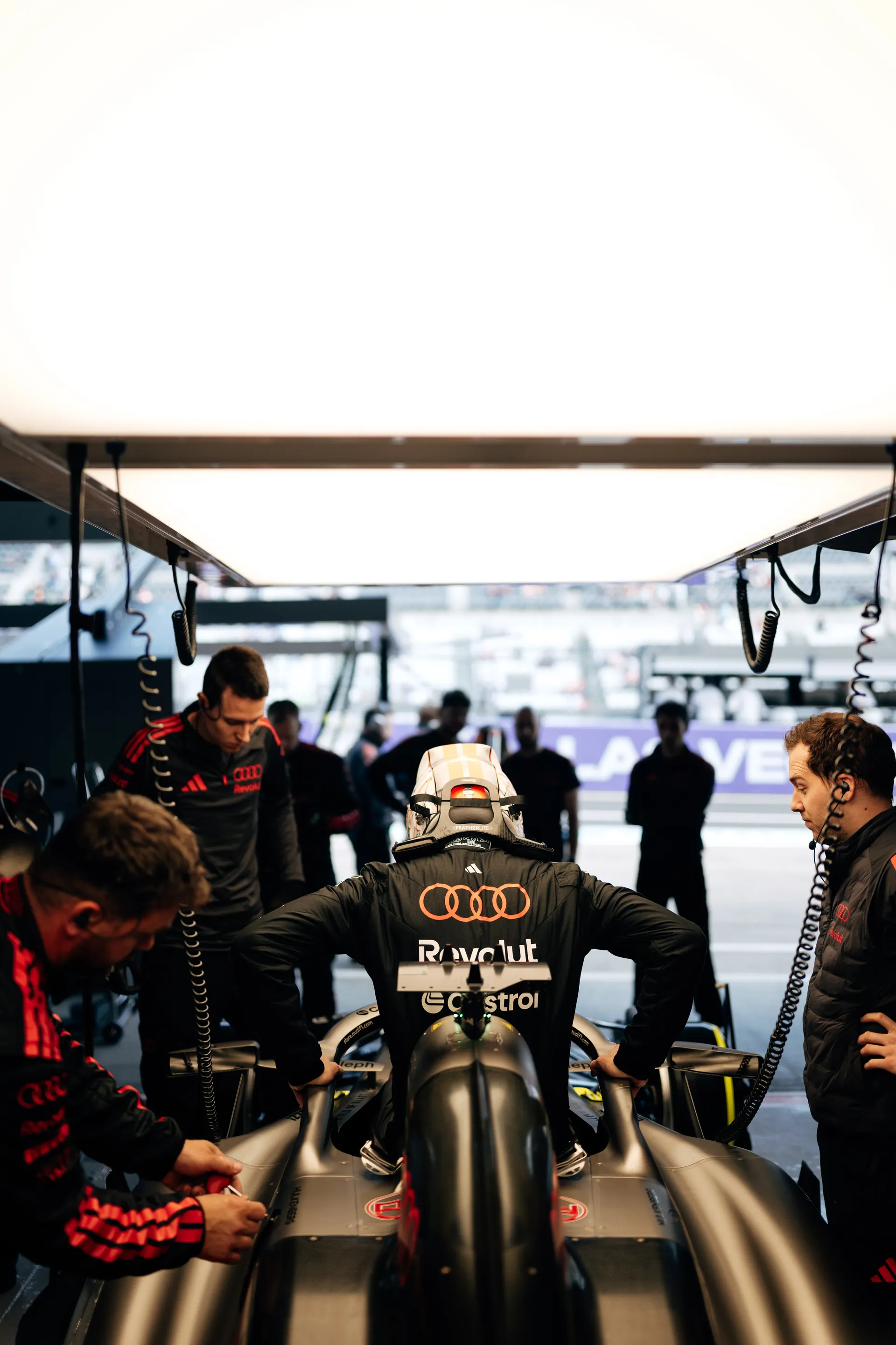 Nico Hulkenberg seated in the Audi Revolut F1® Team car inside the garage while engineers gather around for final checks.