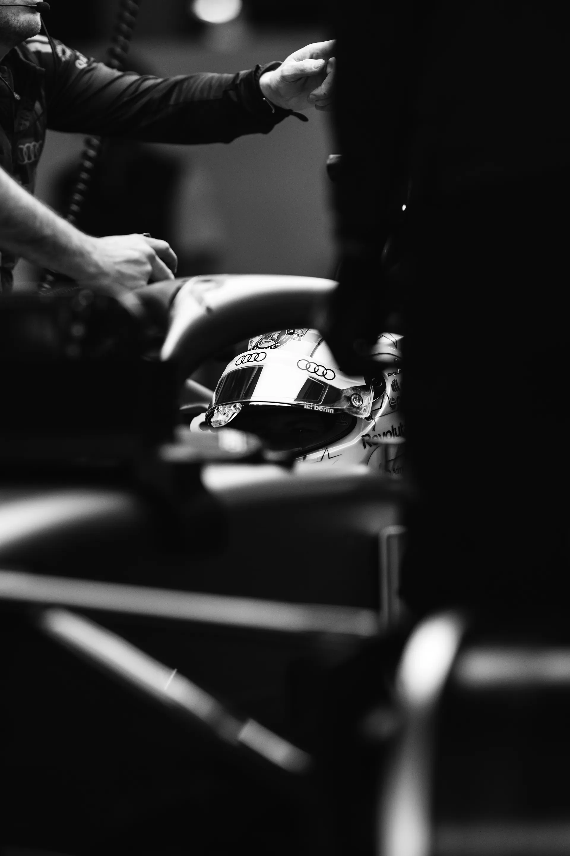 Black and white detail of Nico Hulkenberg's helmet framed by mechanics and cockpit elements inside the garage.