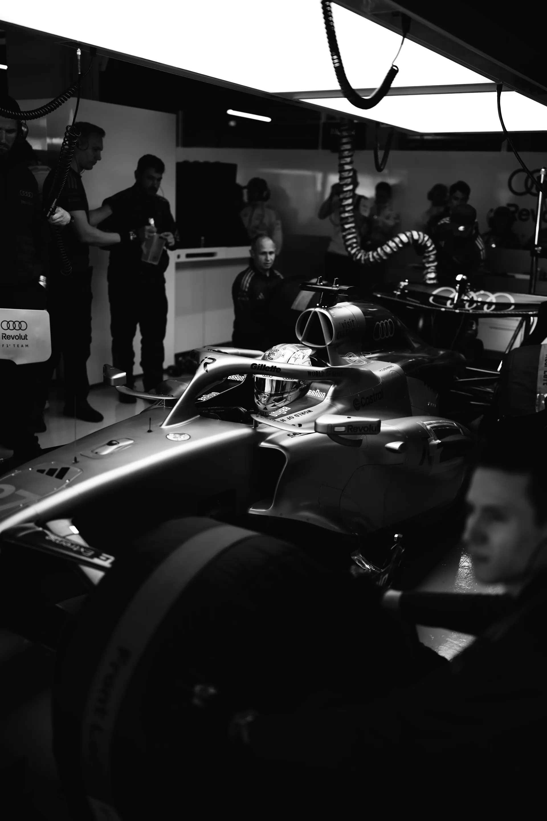 Black and white wide shot of the Audi Revolut F1® Team car in the garage with Nico Hulkenberg in the cockpit and crew surrounding the car.