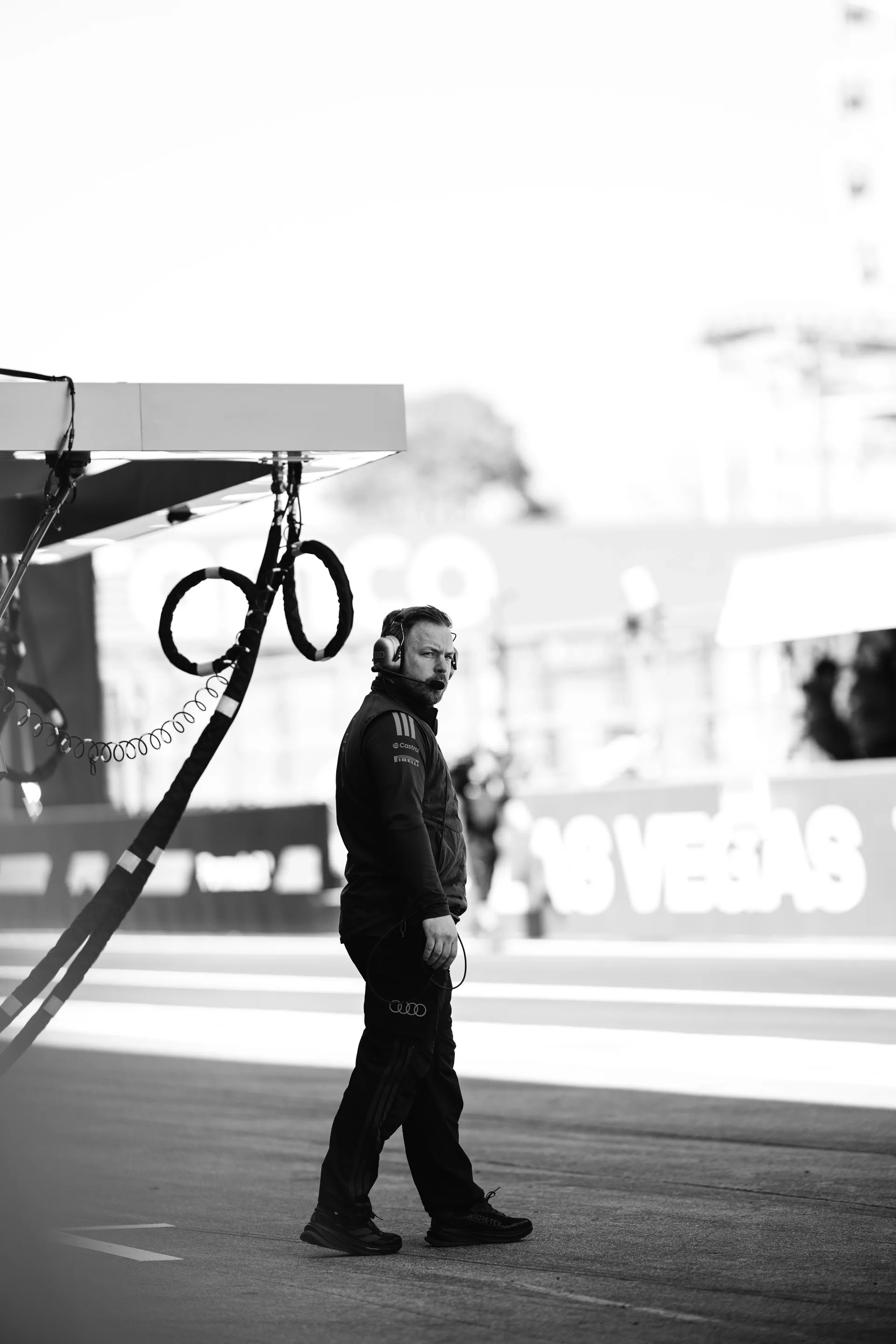 Black and white portrait of a team member wearing a headset and walking along the Suzuka pit lane beside the Audi Revolut F1® Team garage.