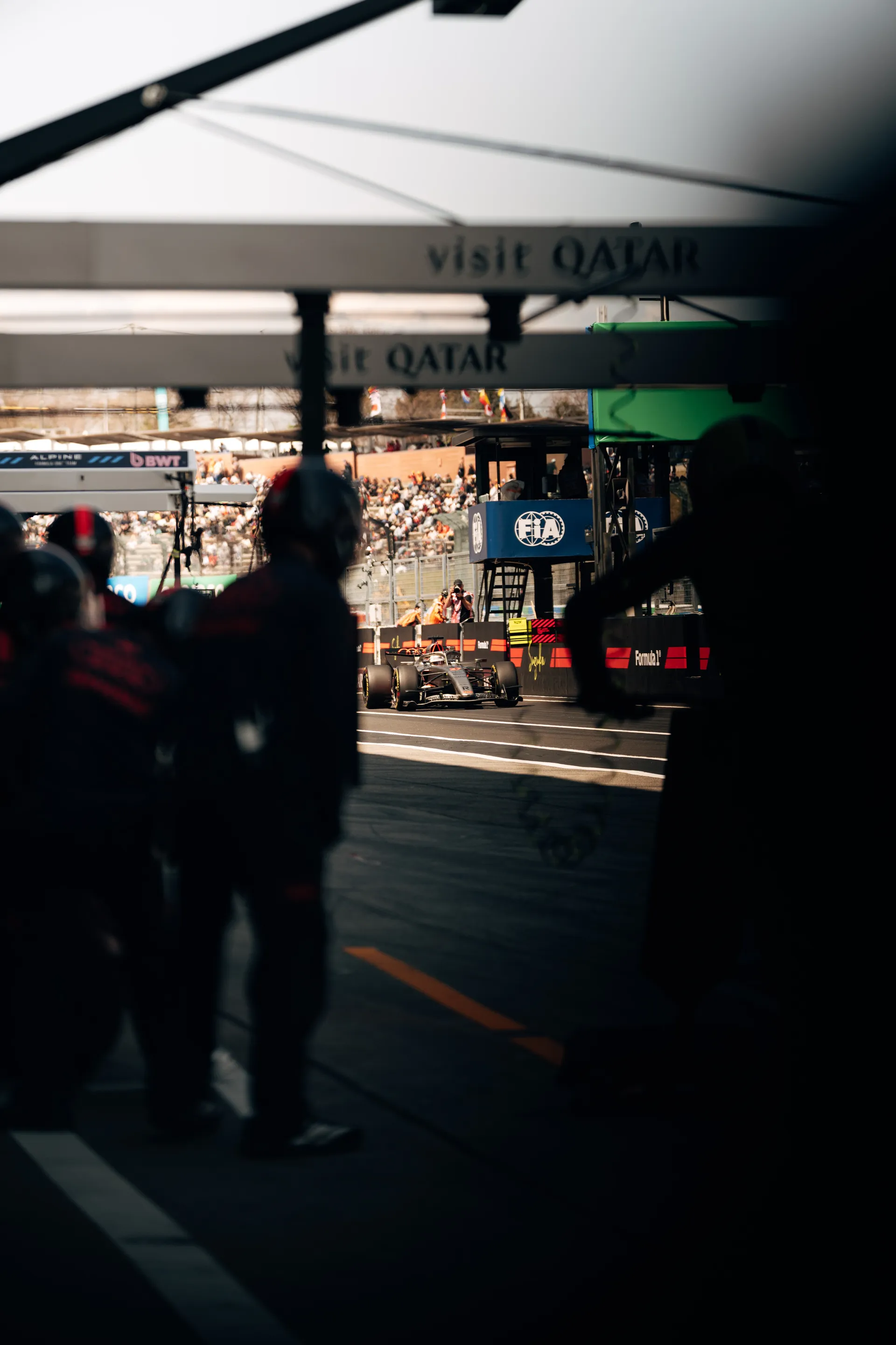 View from inside the Audi Revolut F1® Team garage toward pit lane, with silhouetted crew members in the foreground and an Audi Revolut F1® Team car visible outside near the FIA structure.