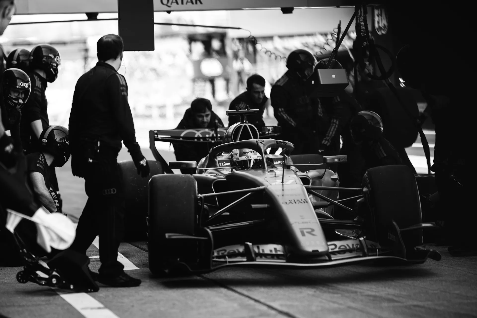 Black and white image of Nico Hulkenberg Audi Revolut F1® Team car in the garage surrounded by mechanics and equipment, prepared for pit lane action.