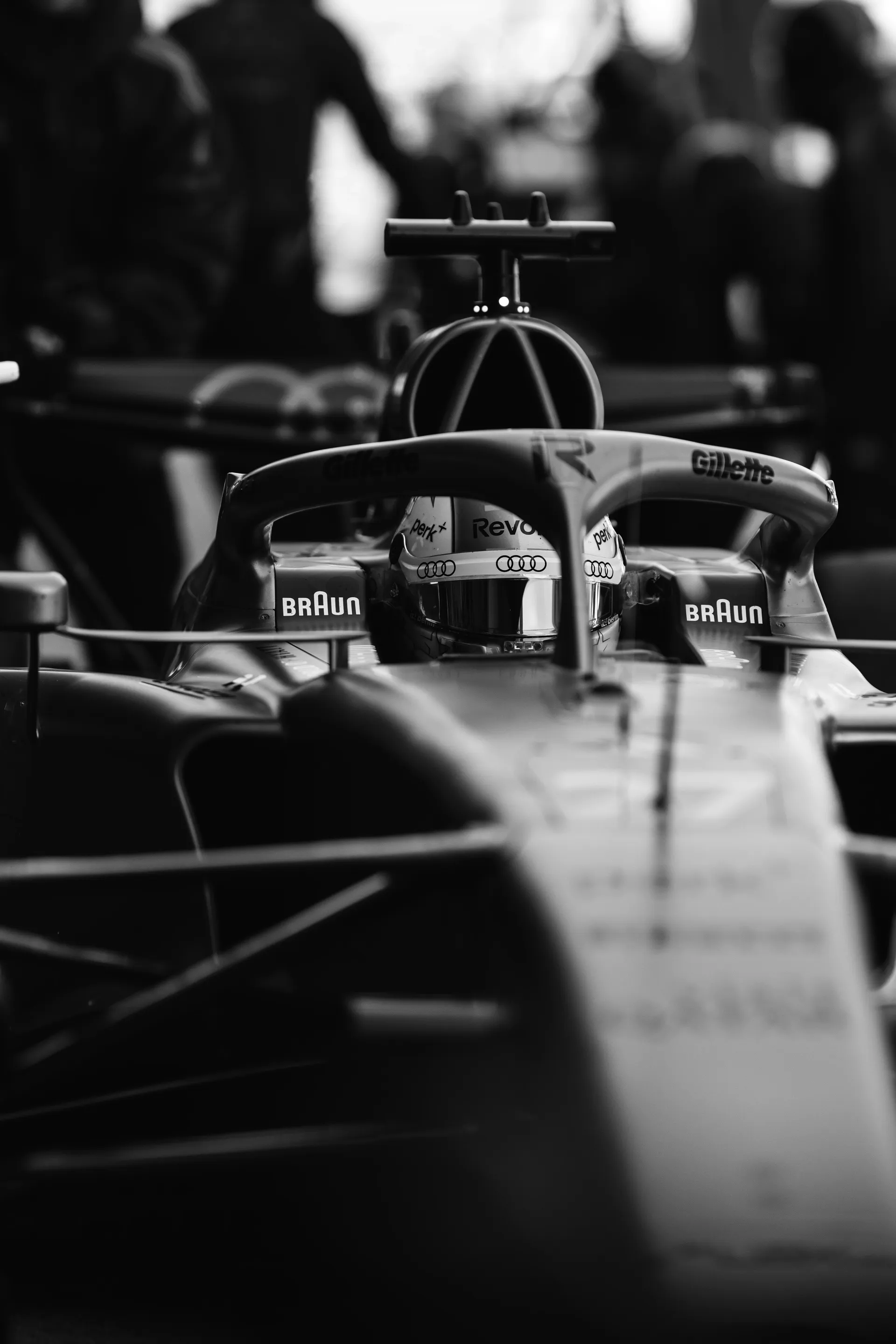 Black and white front facing close up of Nico Hulkenberg sitting in the Audi Revolut F1® Team car, framed by the halo and nose of the car.