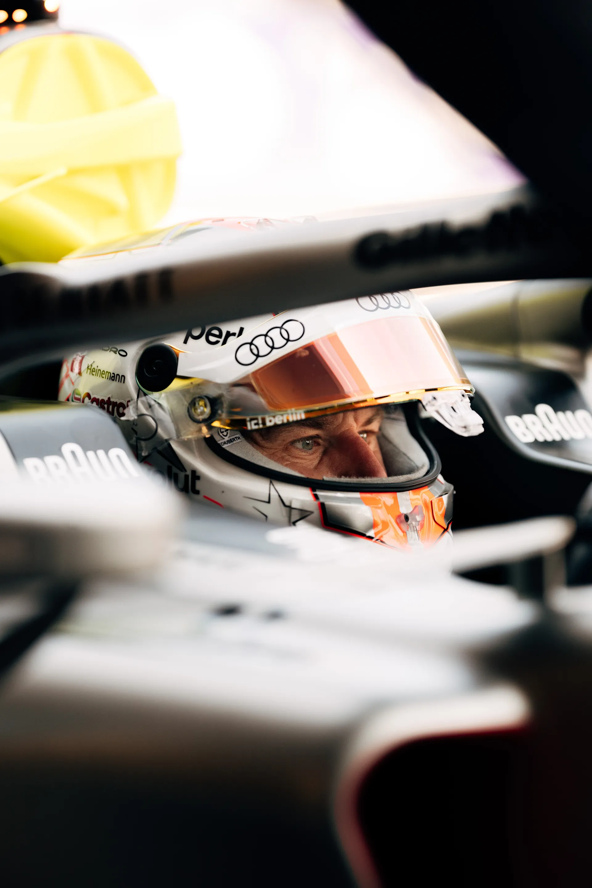 Tight color close up of Nico Hulkenberg inside the cockpit of the Audi Revolut F1® Team car, his eyes visible through the helmet visor as garage equipment frames the shot.