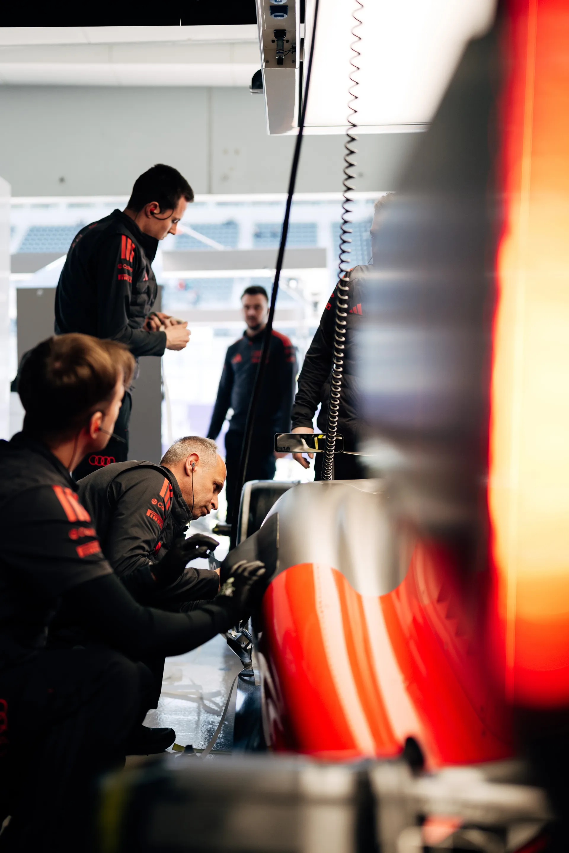Several Audi Revolut F1® Team mechanics gathered around the side of the car in the garage, closely inspecting the bodywork during setup.