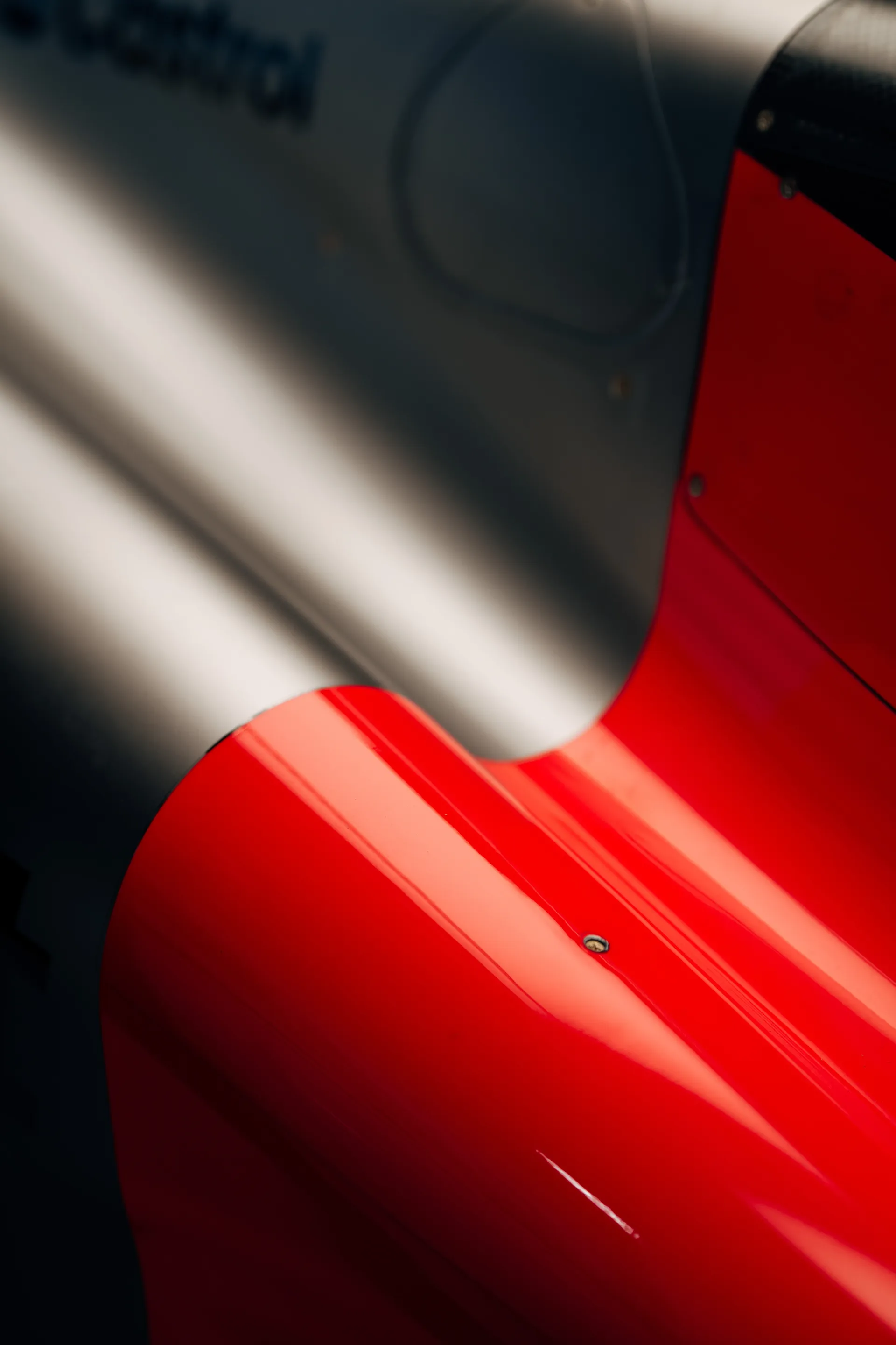 Detail shot of the Audi Revolut F1® Team car bodywork, showing the silver and red surface lines and panel contours in the garage light.