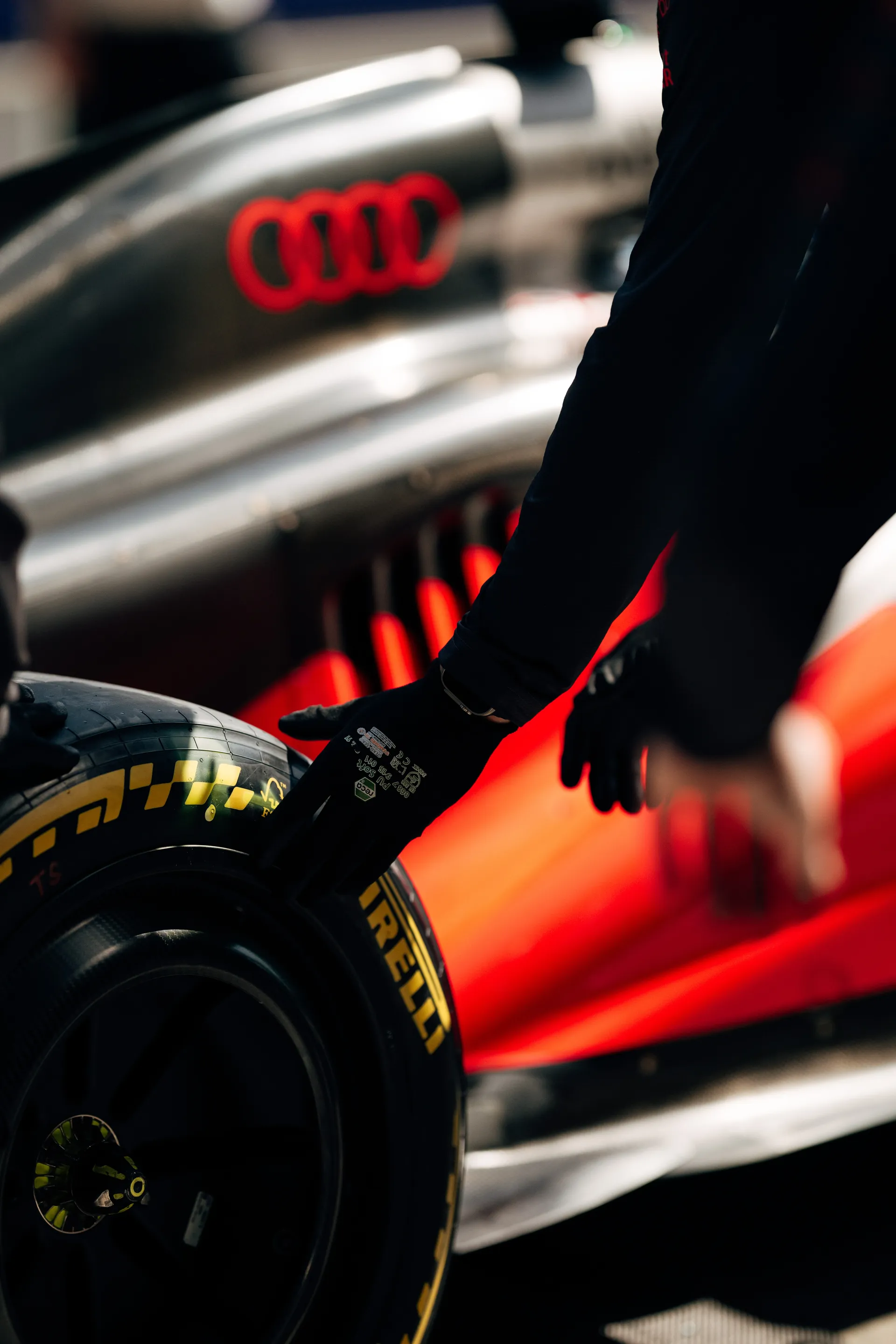 Gloved team member steadying a Pirelli tire beside the red sidepod of the Audi Revolut F1® Team car in the garage.