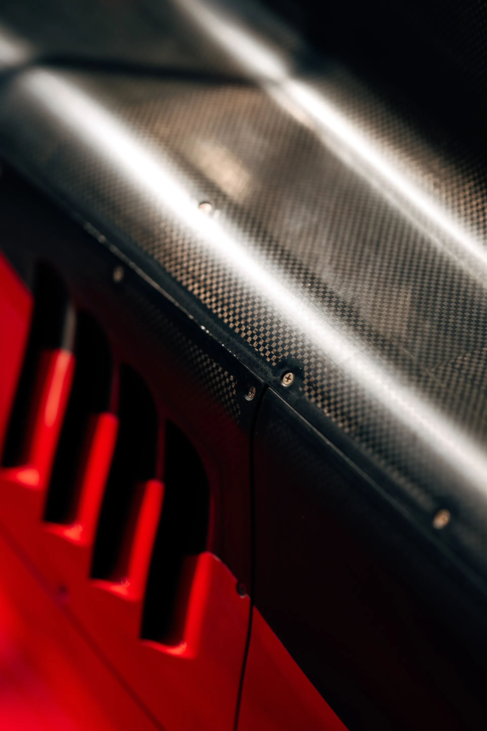 Close up of the Audi Revolut F1® Team car’s carbon fiber bodywork and red vented section under bright garage lighting.