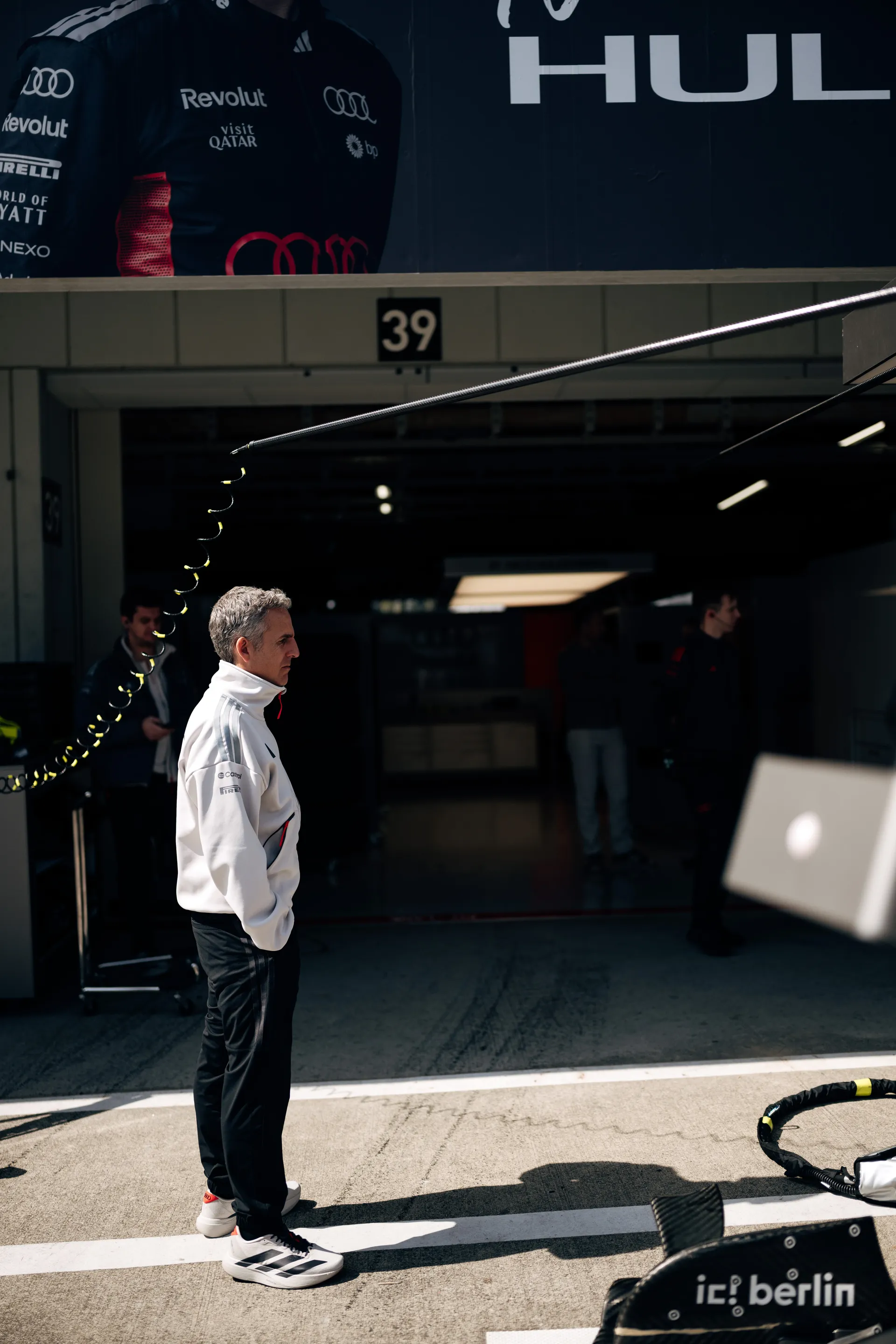 Team member in a white Audi Revolut F1® Team jacket standing in the pit lane outside garage 39, with the Nico Hulkenberg garage banner above.