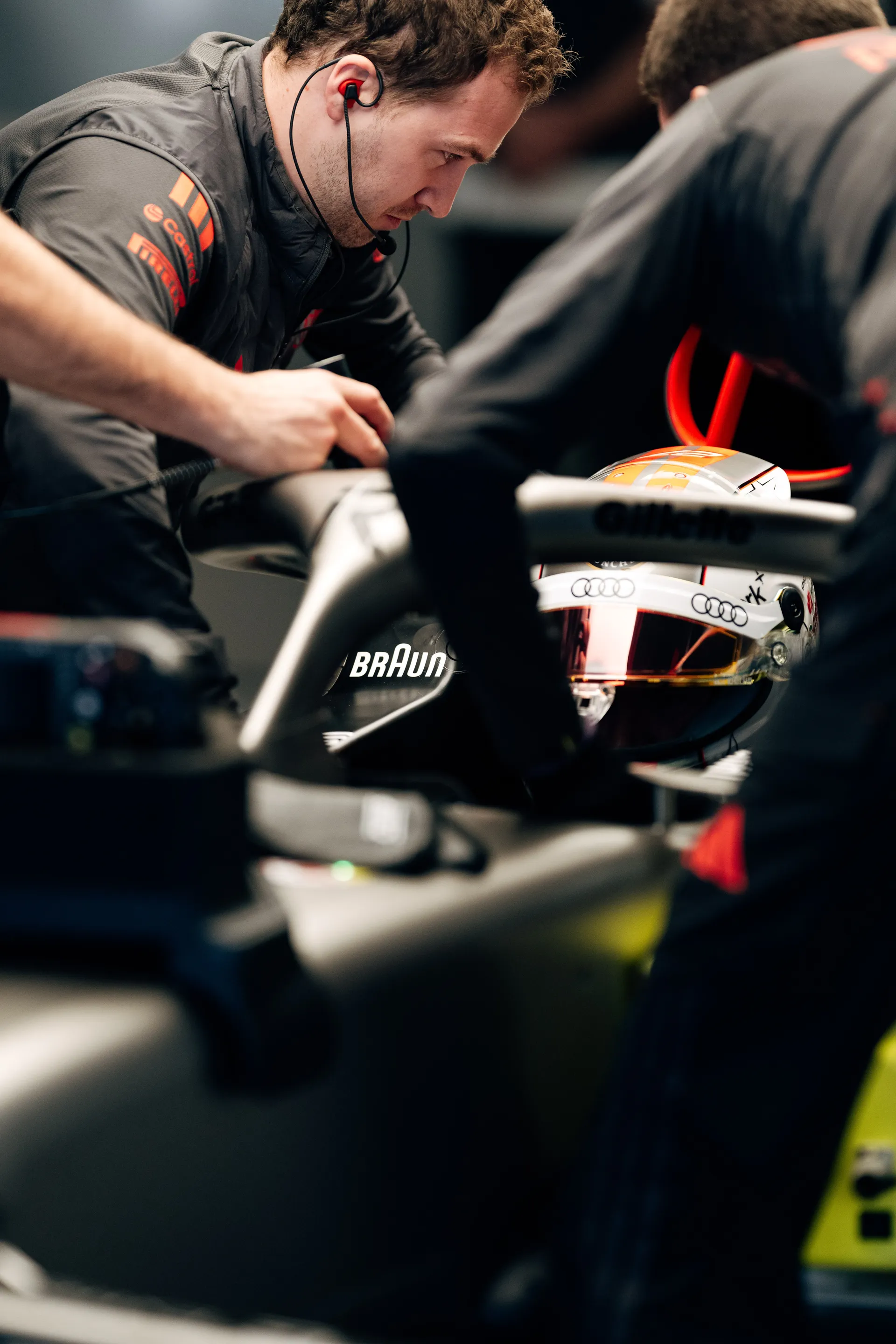 Audi Revolut F1® Team mechanics working around Nico Hulkenberg in the cockpit, with his helmet visible as final adjustments are made in the garage.