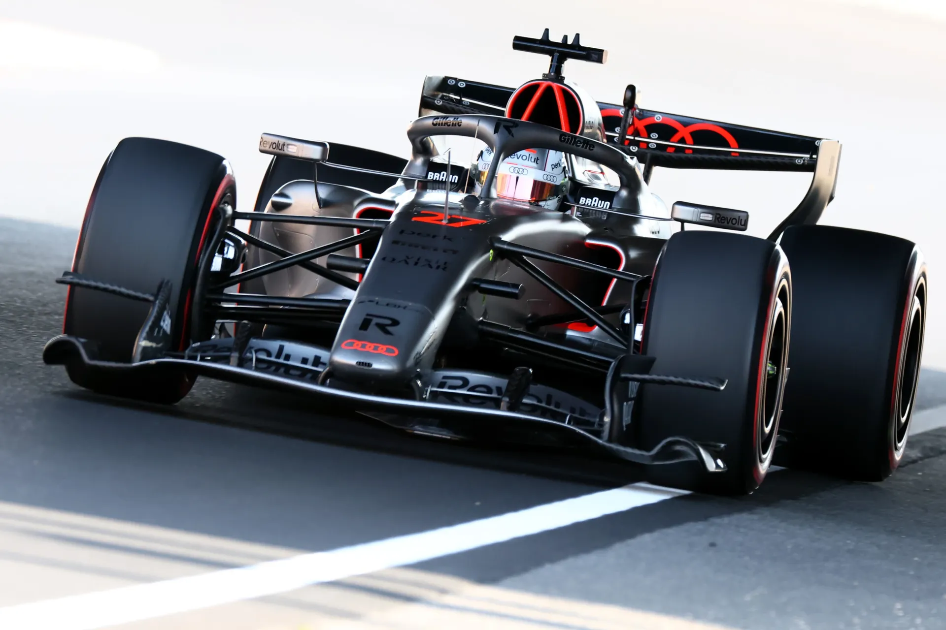 Front three quarter view of an Audi Revolut F1® Team Formula 1 car on track at Suzuka, with the illuminated red Audi rings and black silver bodywork clearly visible.