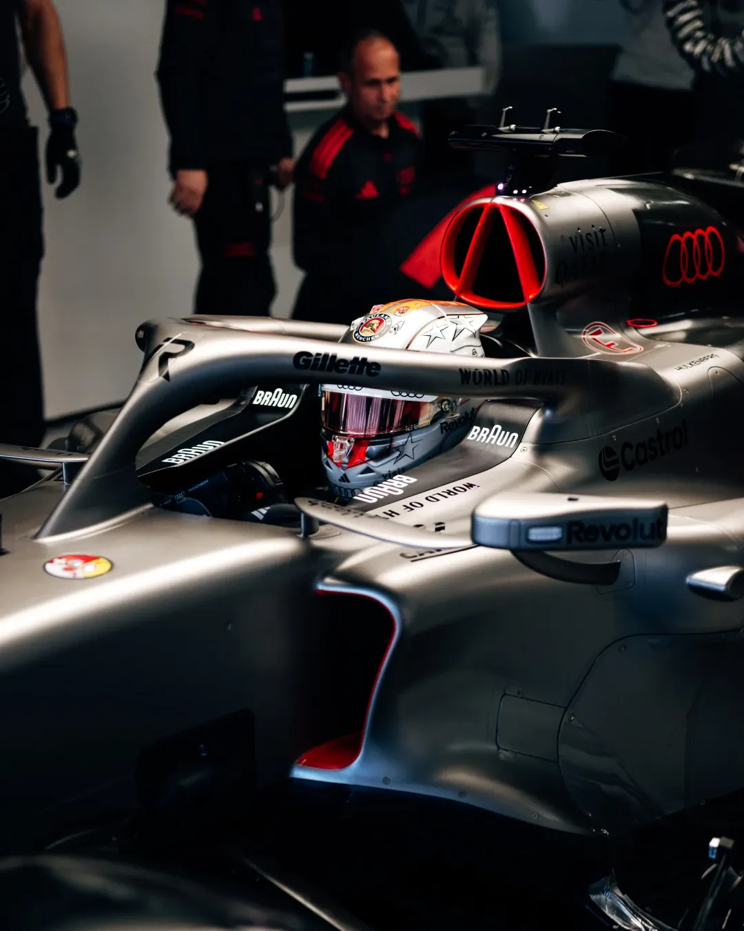 Nico Hulkenberg sits in the Audi Revolut F1® Team car inside the garage during FP3 in Japan, seen in profile through the halo with the silver bodywork and red-lit air intake standing out behind him.