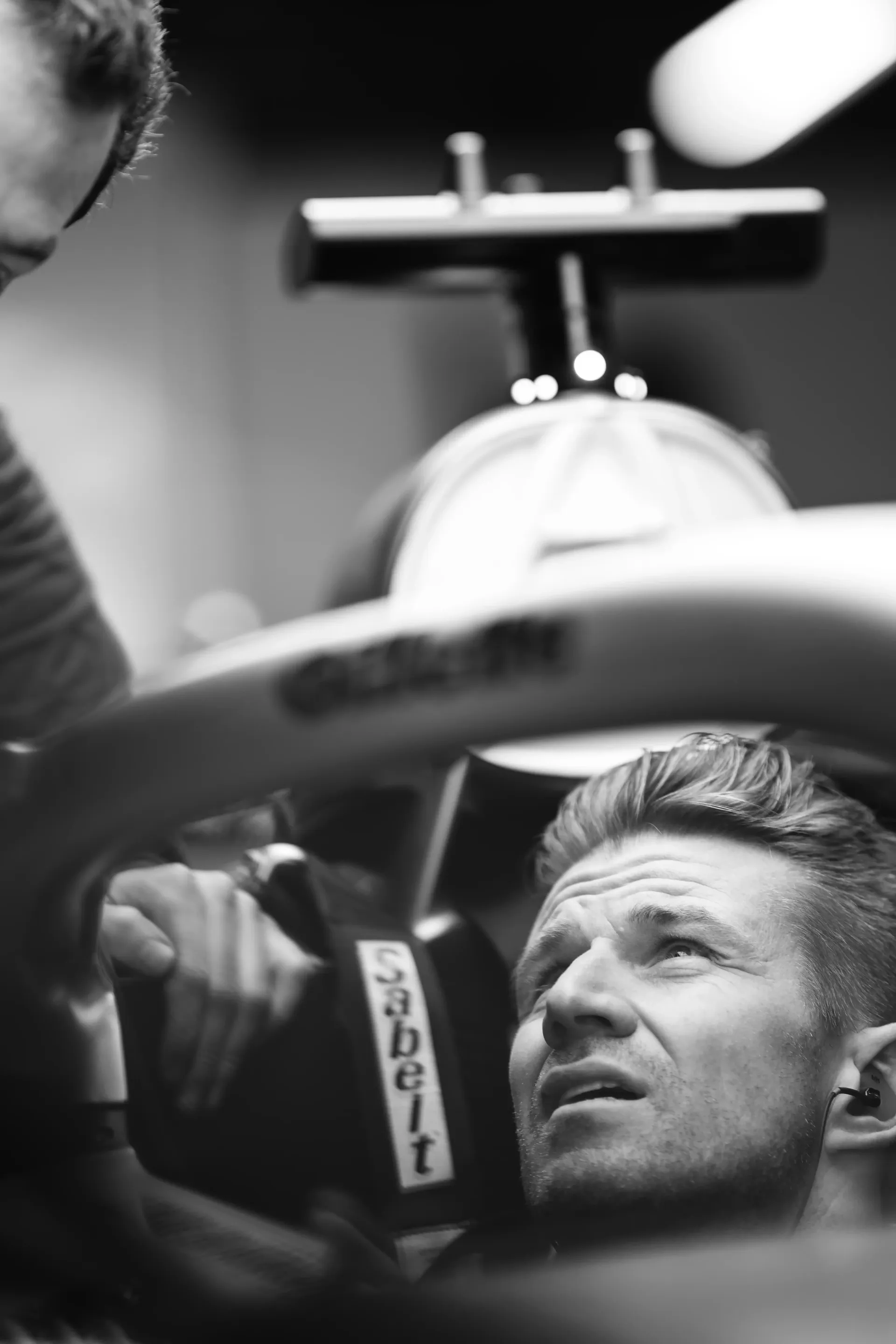 Black-and-white close-up of Audi F1® team driver Nico Hulkenberg in cockpit of his R26 car in garage during Suzuka F1® race weekend setup.