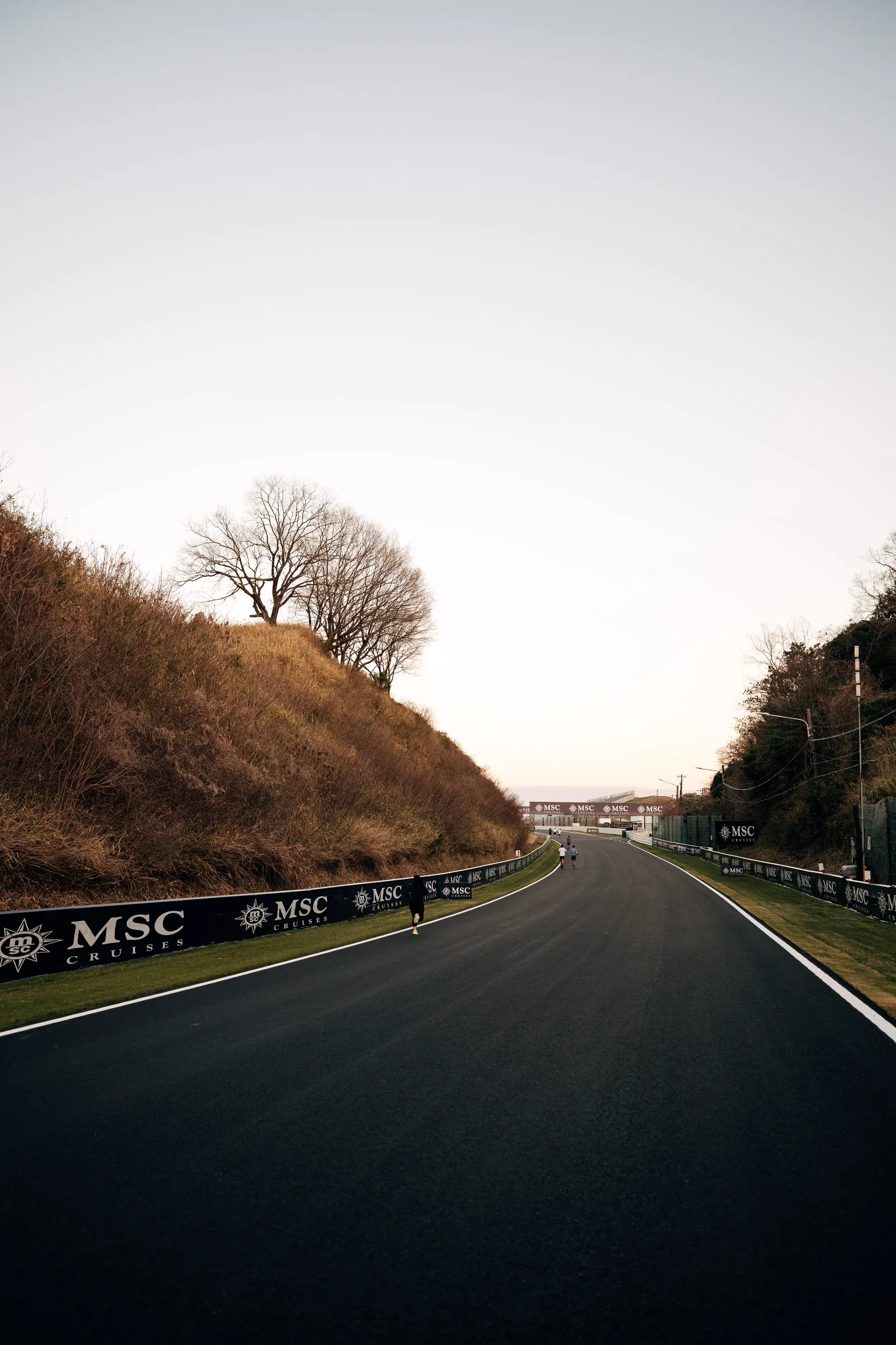 Wide view of the Suzuka circuit with runners spread out along the track during an evening track walk.