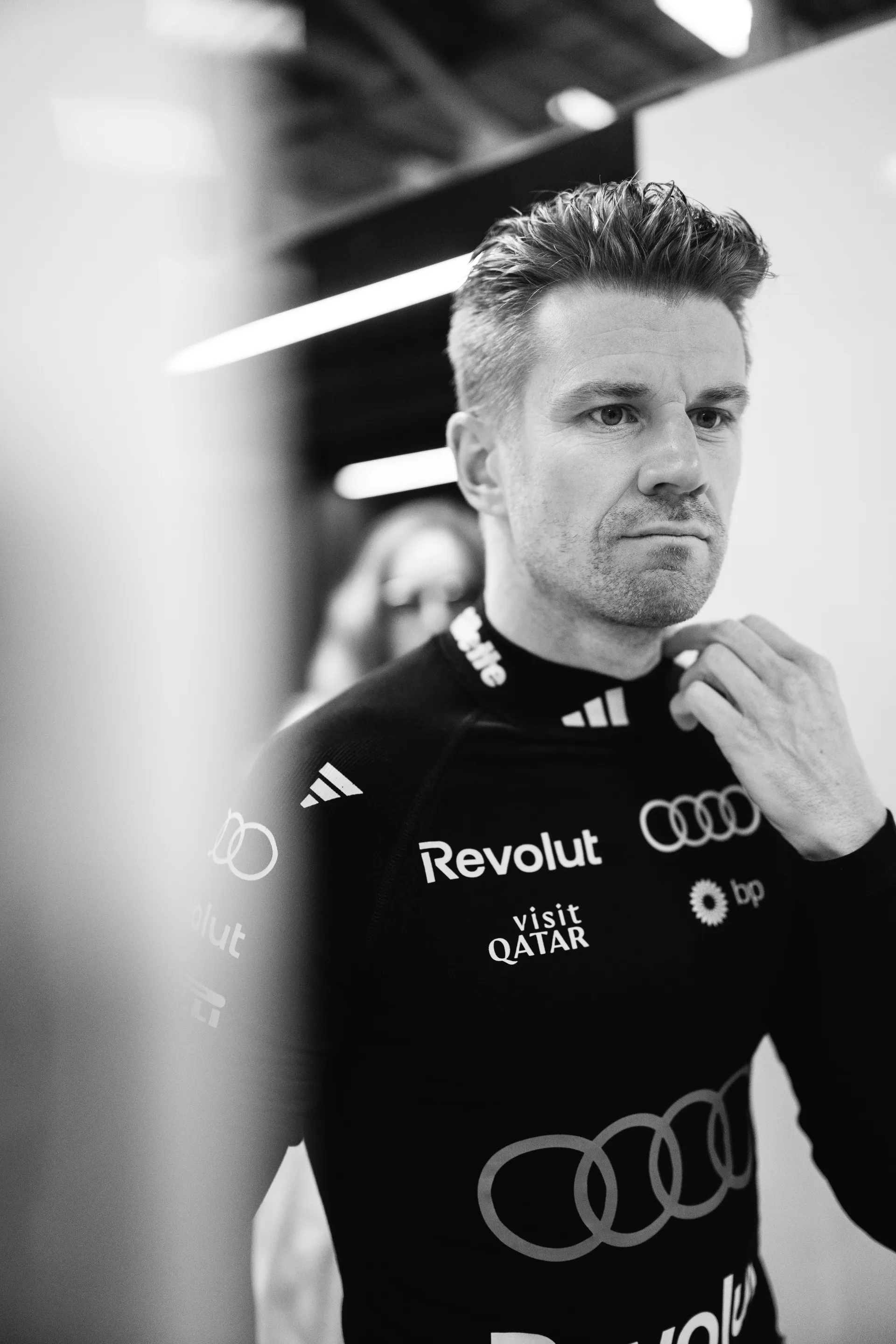 Close black and white portrait of Nico Hulkenberg adjusting his race top in the Audi Revolut F1® Team garage before qualifying.