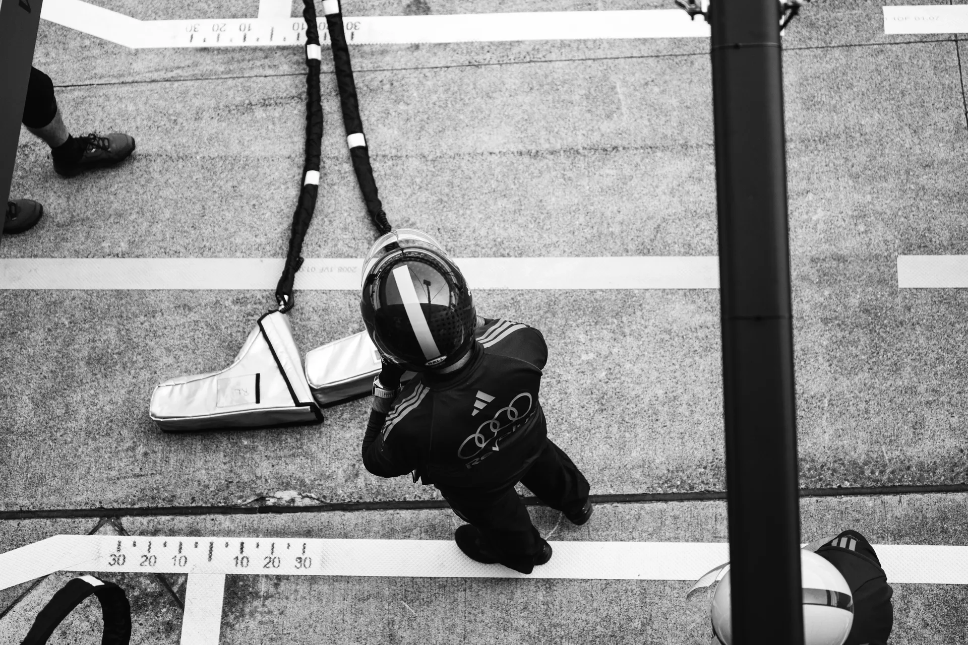 Overhead black and white image of an Audi Revolut F1® Team crew member in helmet and race gear standing in the pit lane beside equipment during qualifying.