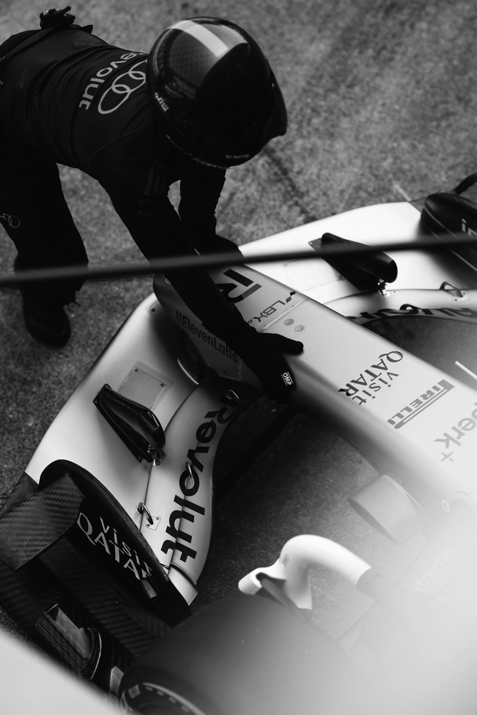 Black and white overhead close up of an Audi Revolut F1® Team crew member leaning over the car’s nose and front wing in the pit lane.