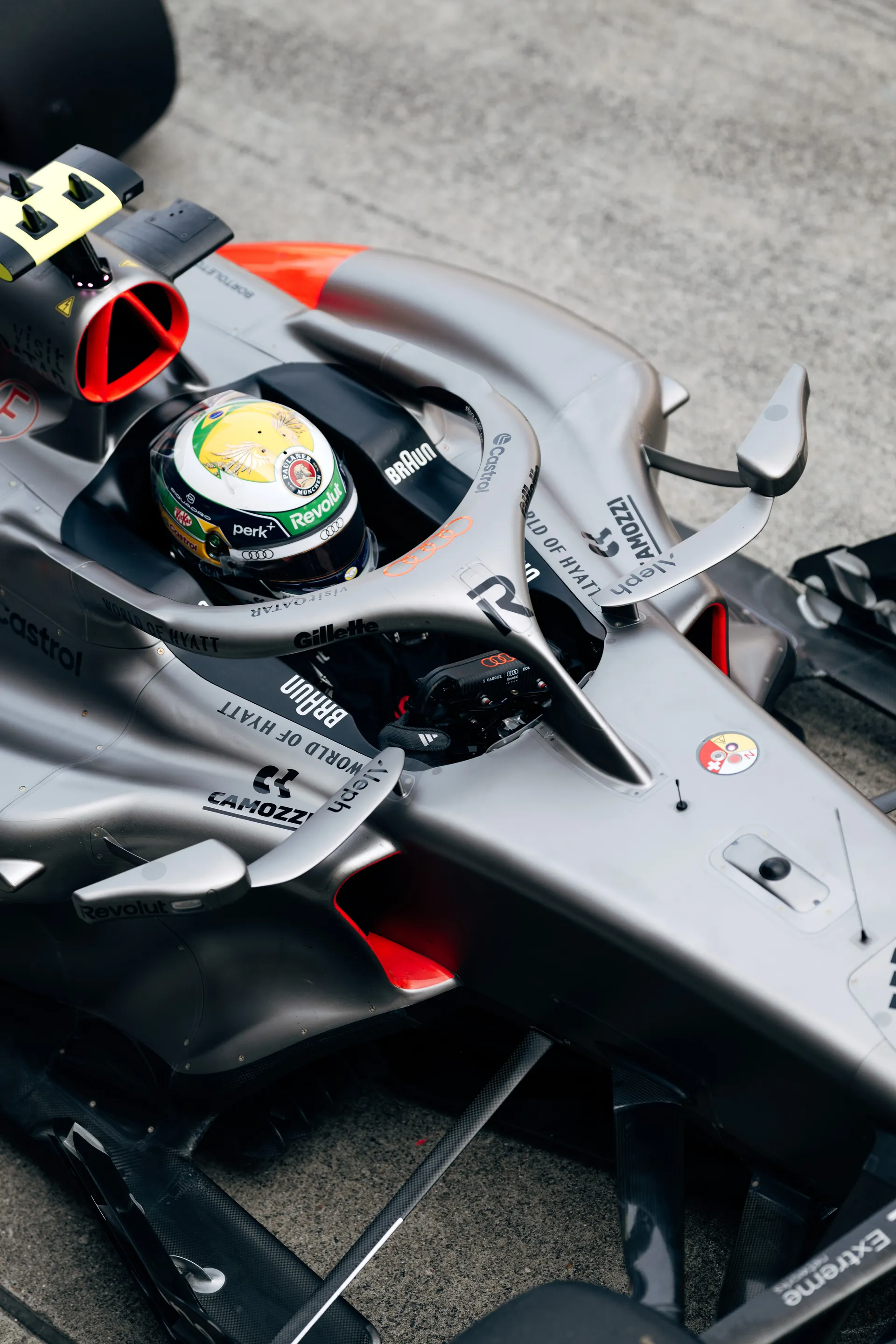 Top down detail of Gabriel Bortoleto seated in the Audi Revolut F1® Team car, identified by his yellow and green helmet design, as the car waits in the pit lane.