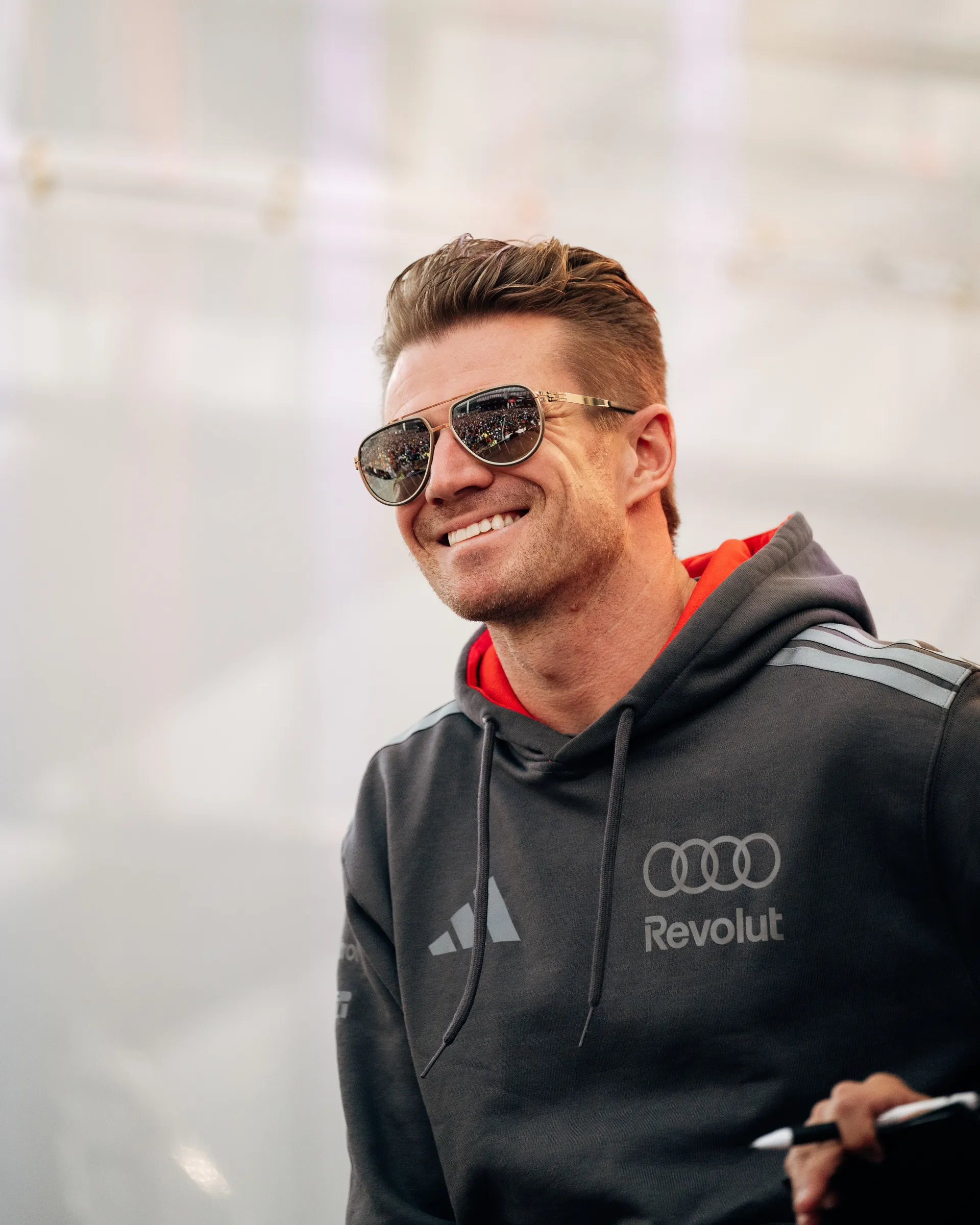 Close portrait of Nico Hulkenberg smiling in sunglasses while wearing an Audi Revolut F1® Team hoodie.