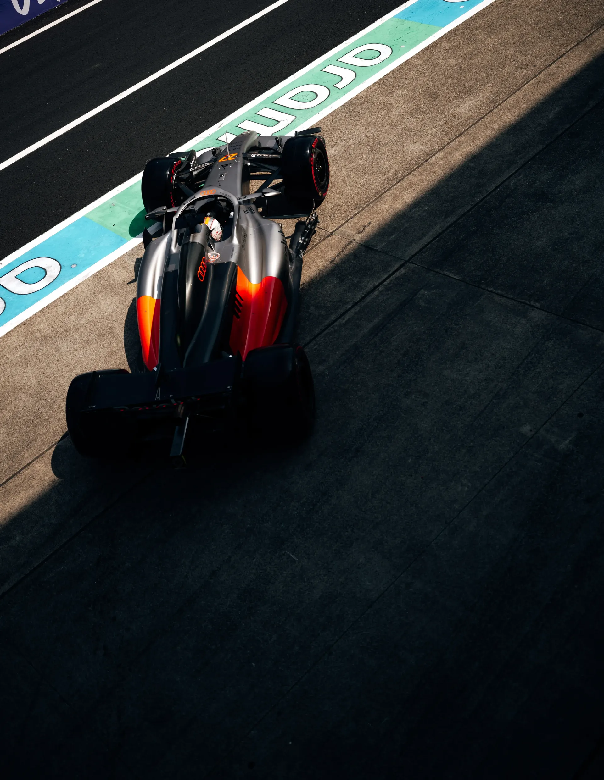 High angle shot of an Audi Revolut F1® Team car running along the Suzuka pit lane near the turquoise lane markings.