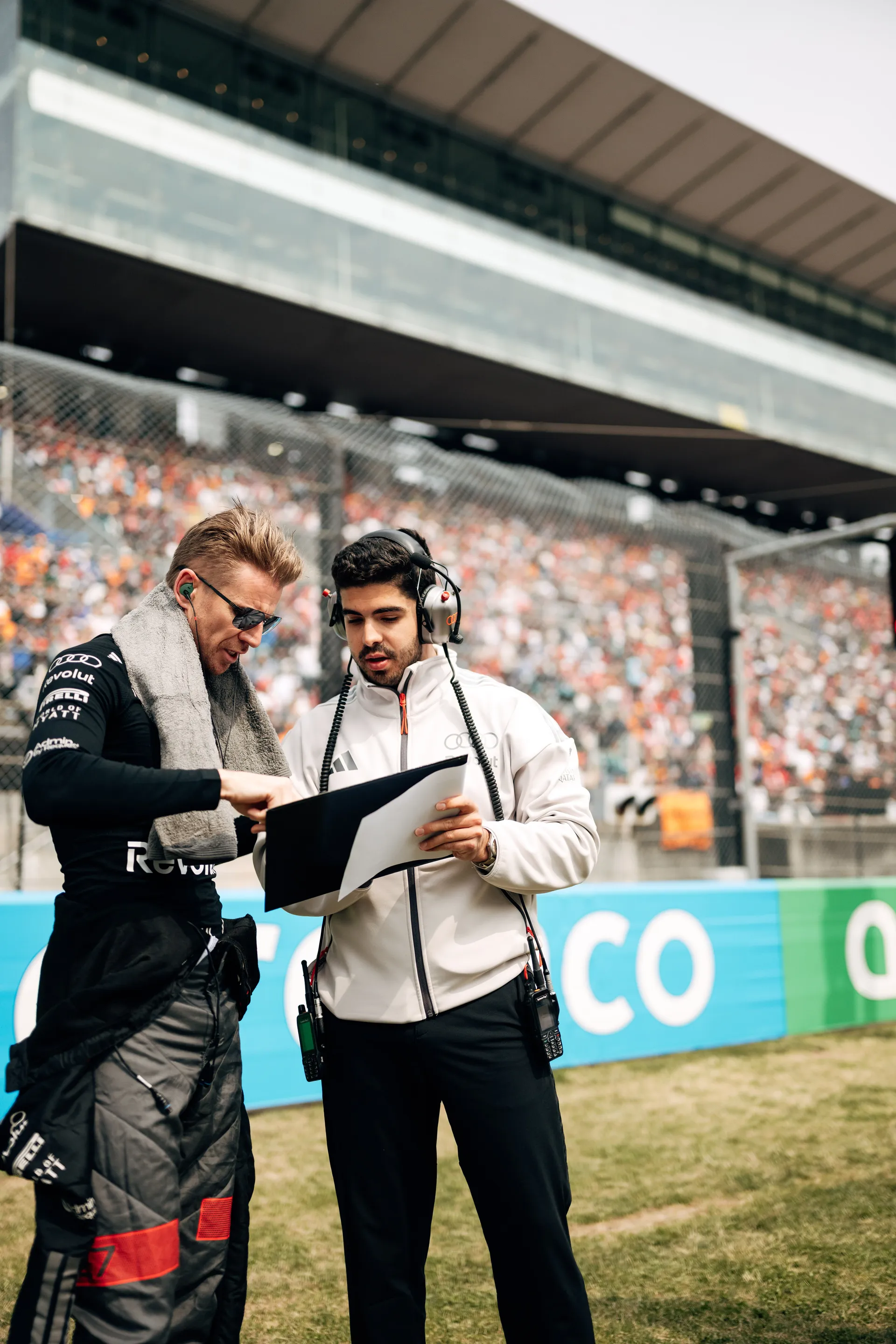 Nico Hulkenberg reviews a document with a team engineer at trackside in front of the grandstands.