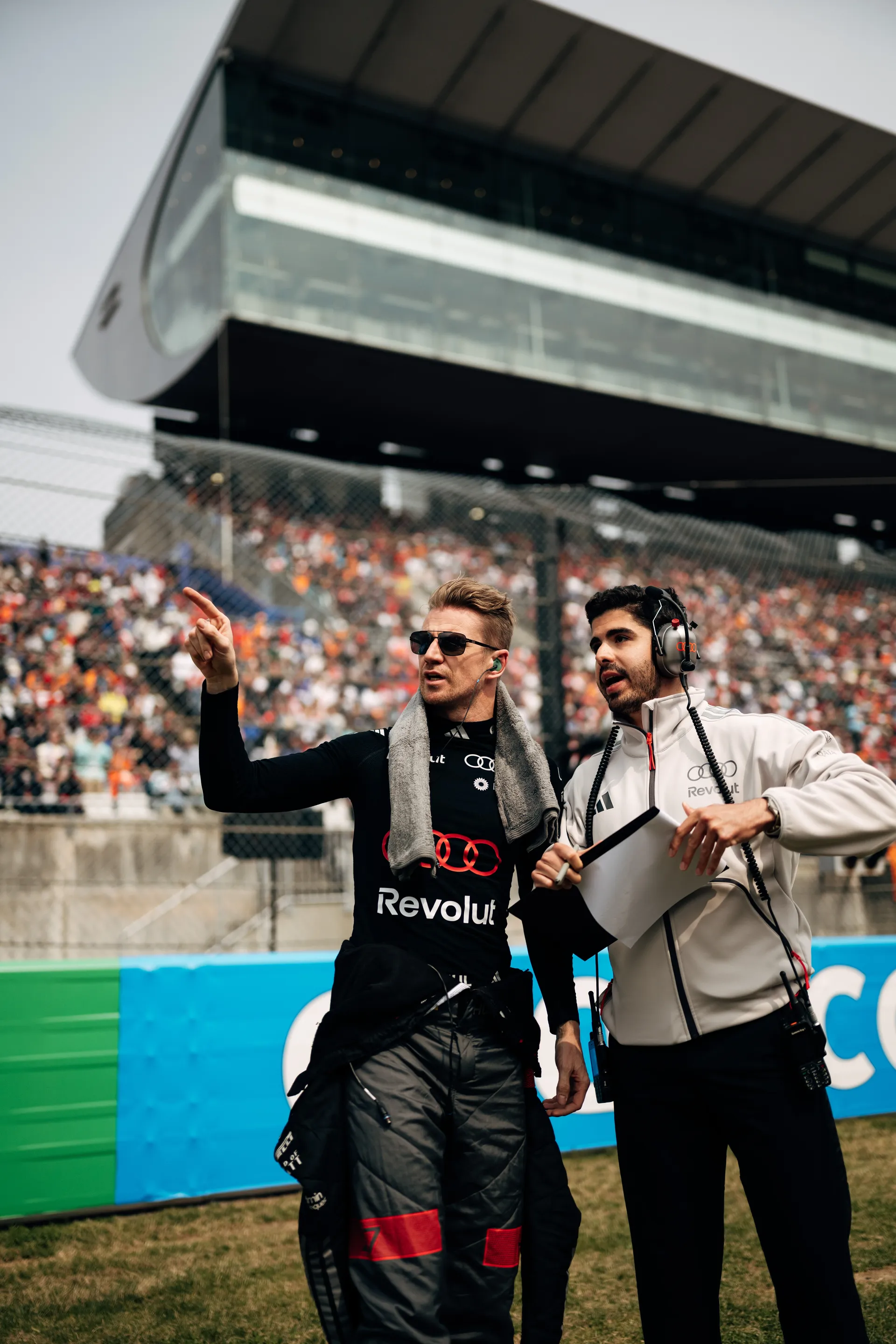 Nico Hulkenberg points toward the track while speaking with a team engineer holding a clipboard.