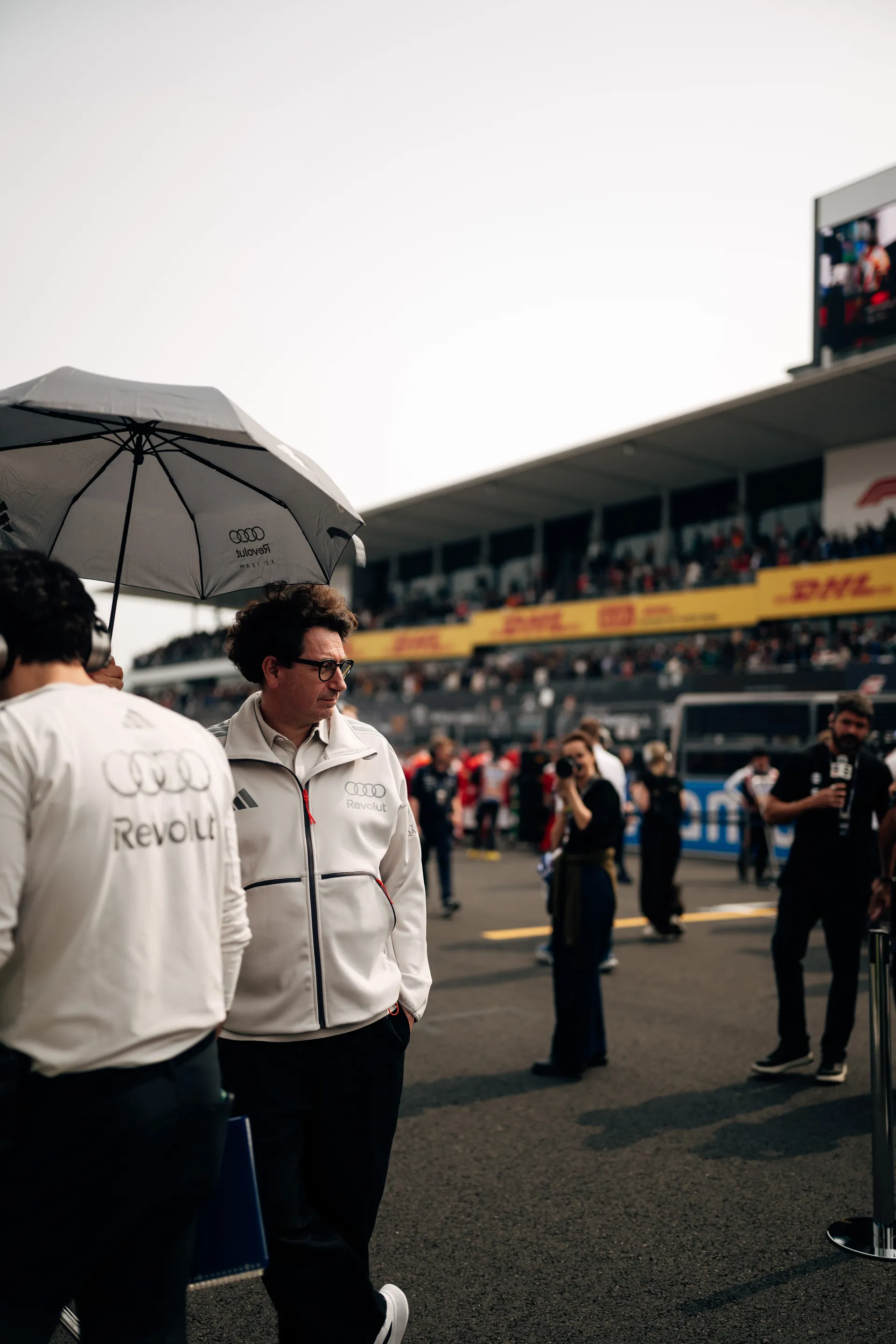 Mattia Binotto stands on the grid in front of the pit building during the pre race lineup.