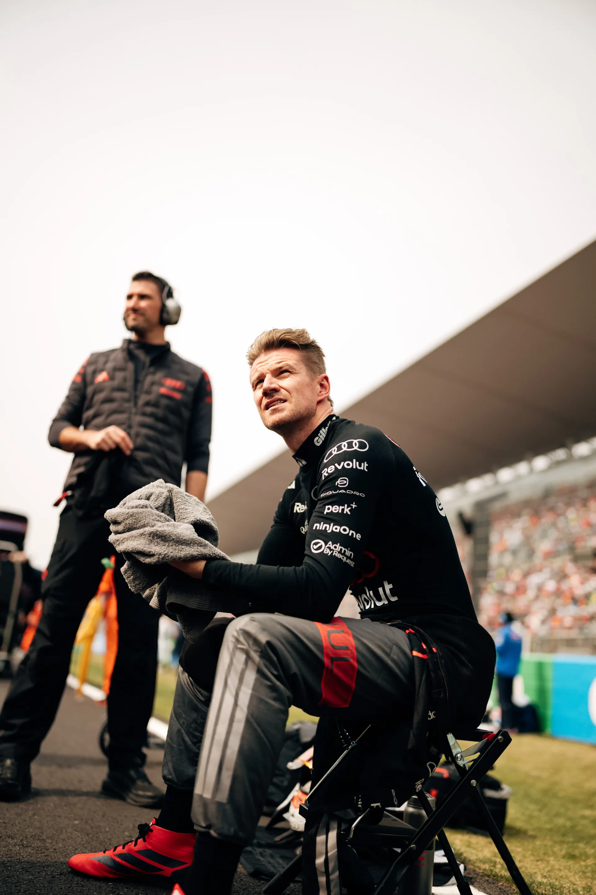 Nico Hulkenberg sits trackside with a towel in hand while looking toward the circuit.