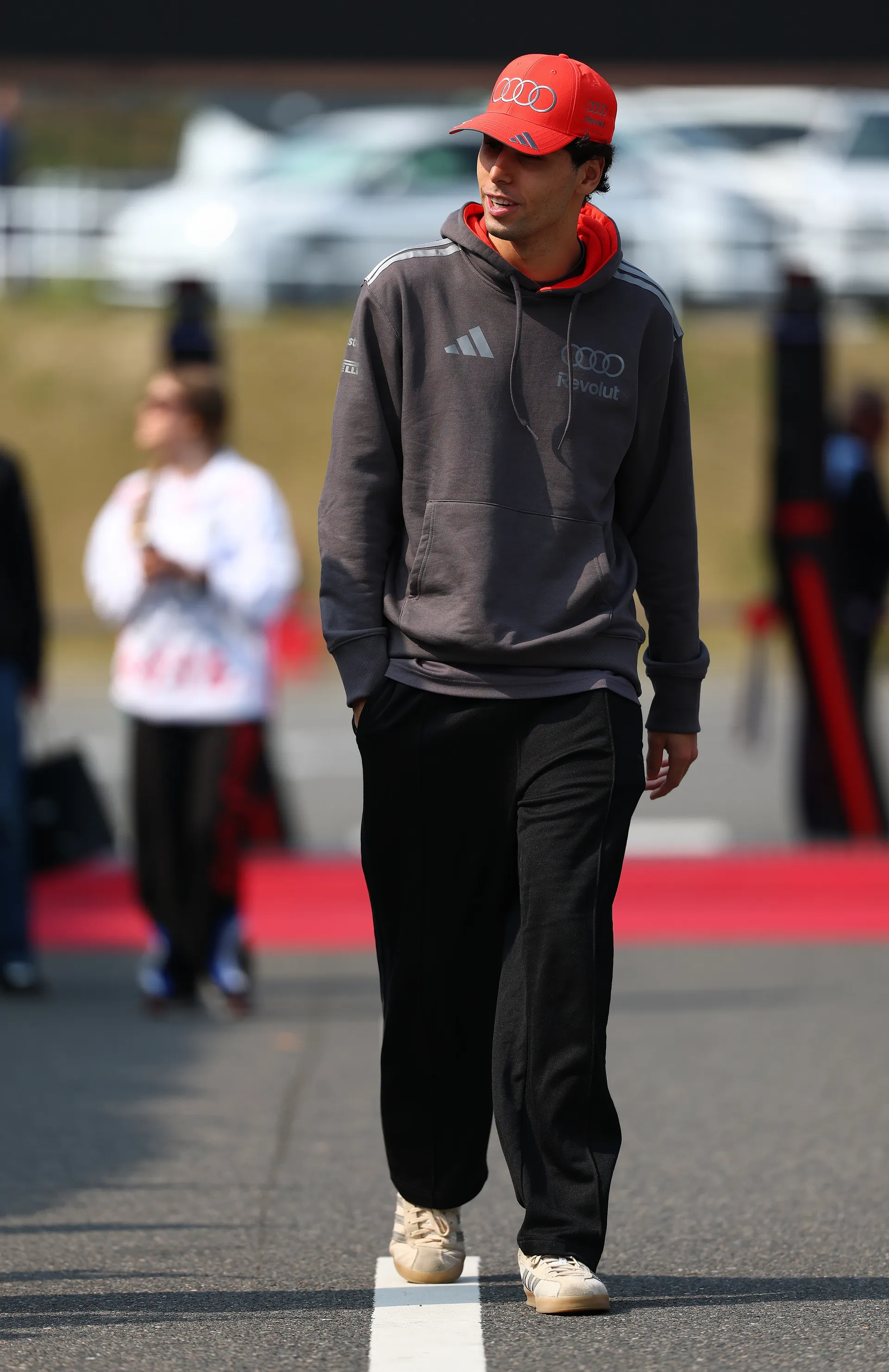 Gabriel Bortoleto of Audi Revolut F1® Team walks along the track in a gray team hoodie, black trousers, and a red cap during the Japanese Grand Prix weekend.