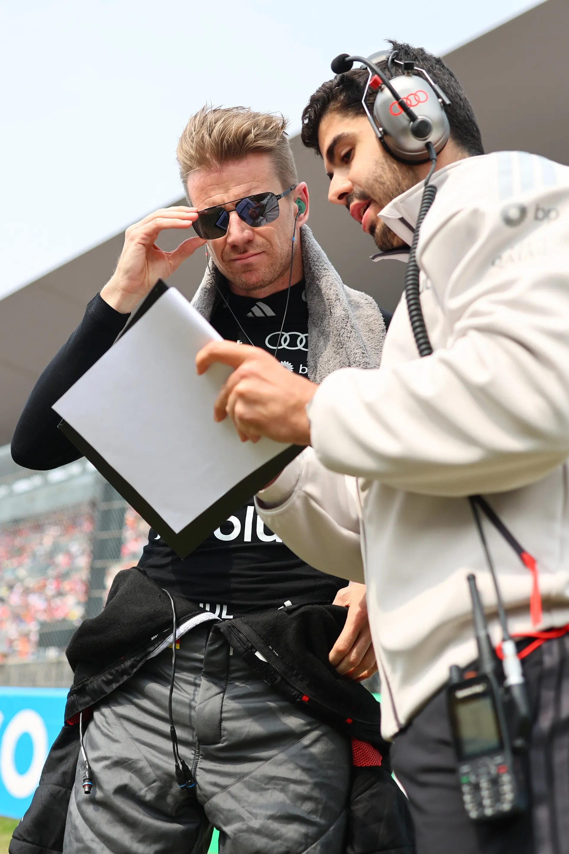 Nico Hulkenberg of Audi Revolut F1® Team reviews notes with a team engineer wearing a headset on the grid before the session.