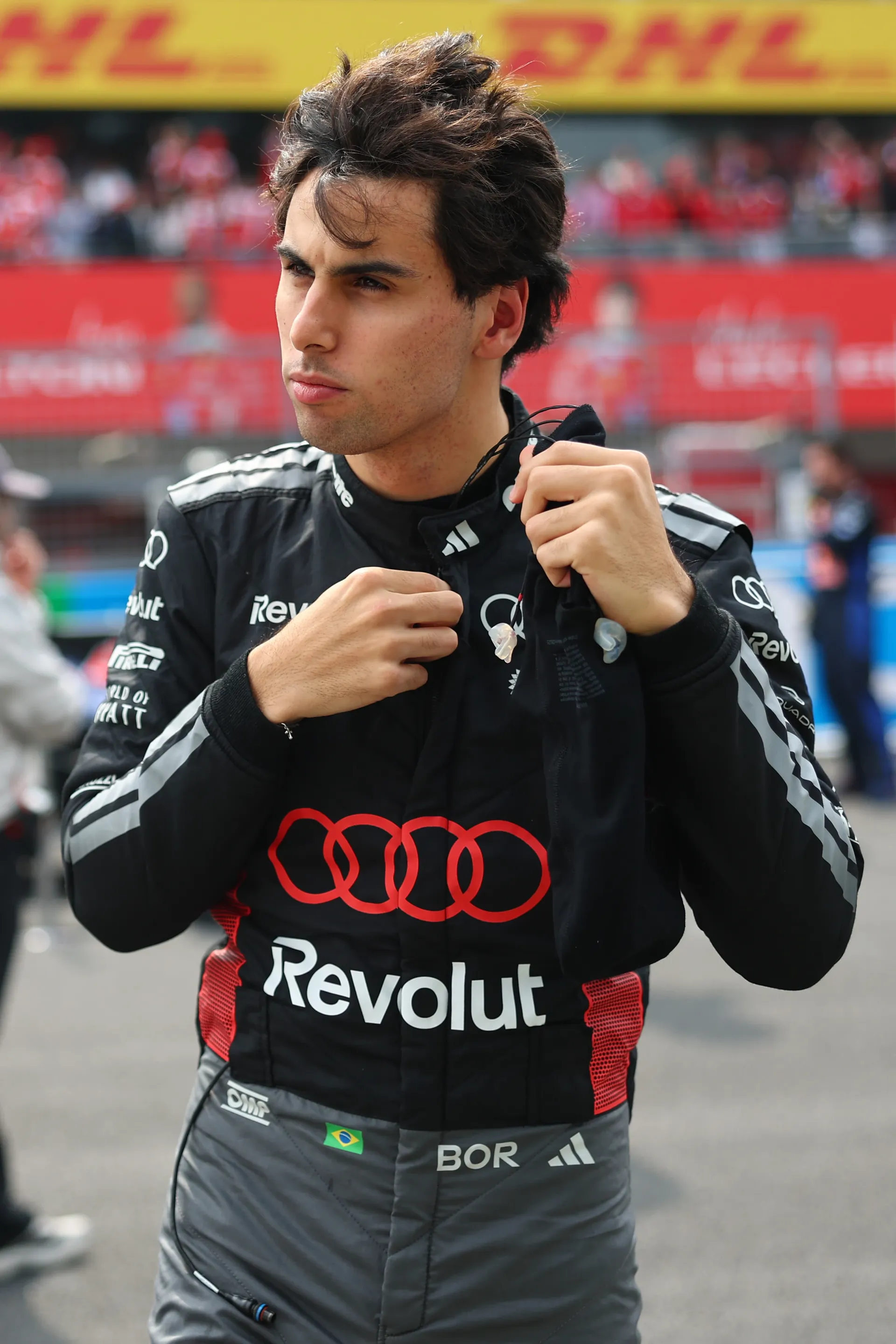 Gabriel Bortoleto of Audi Revolut F1® Team adjusts his earpieces on the grid with the Suzuka grandstands blurred in the background.