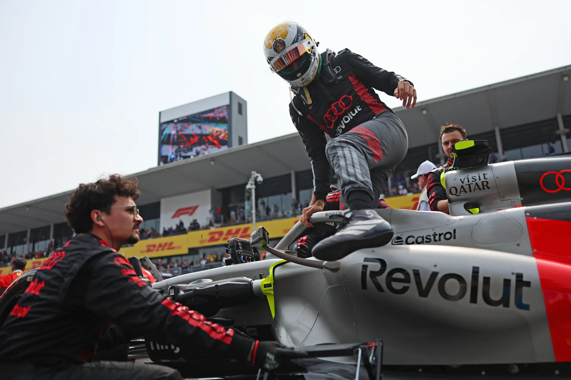 Gabriel Bortoleto of Audi Revolut F1® Team steps out of his car in full race gear as crew members gather around on the grid at Suzuka.