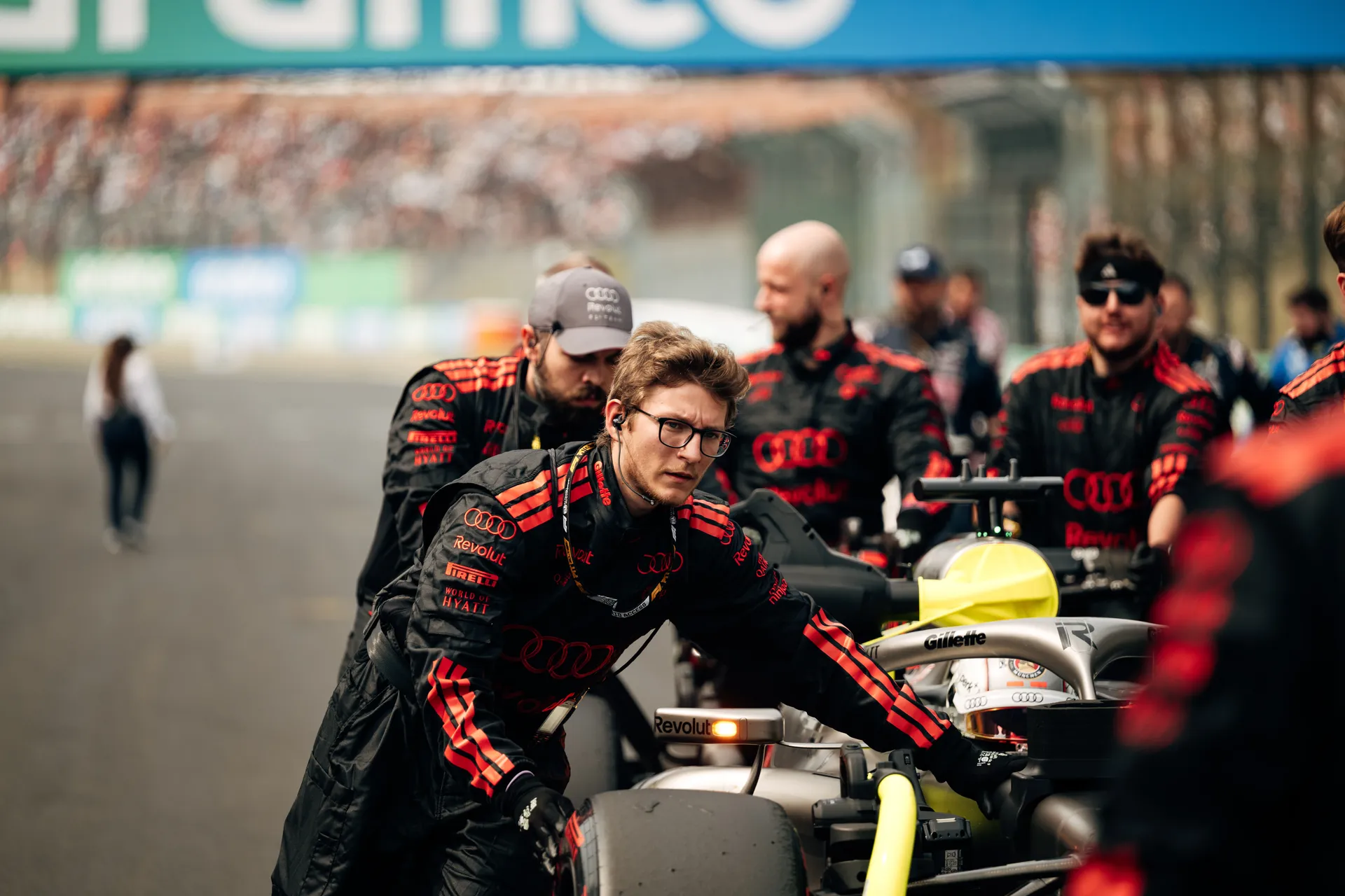 Audi Revolut F1® Team crew members push Gabriel Bortoleto’s car along the grid beneath the Aramco signage, with one mechanic in sharp focus in the foreground.