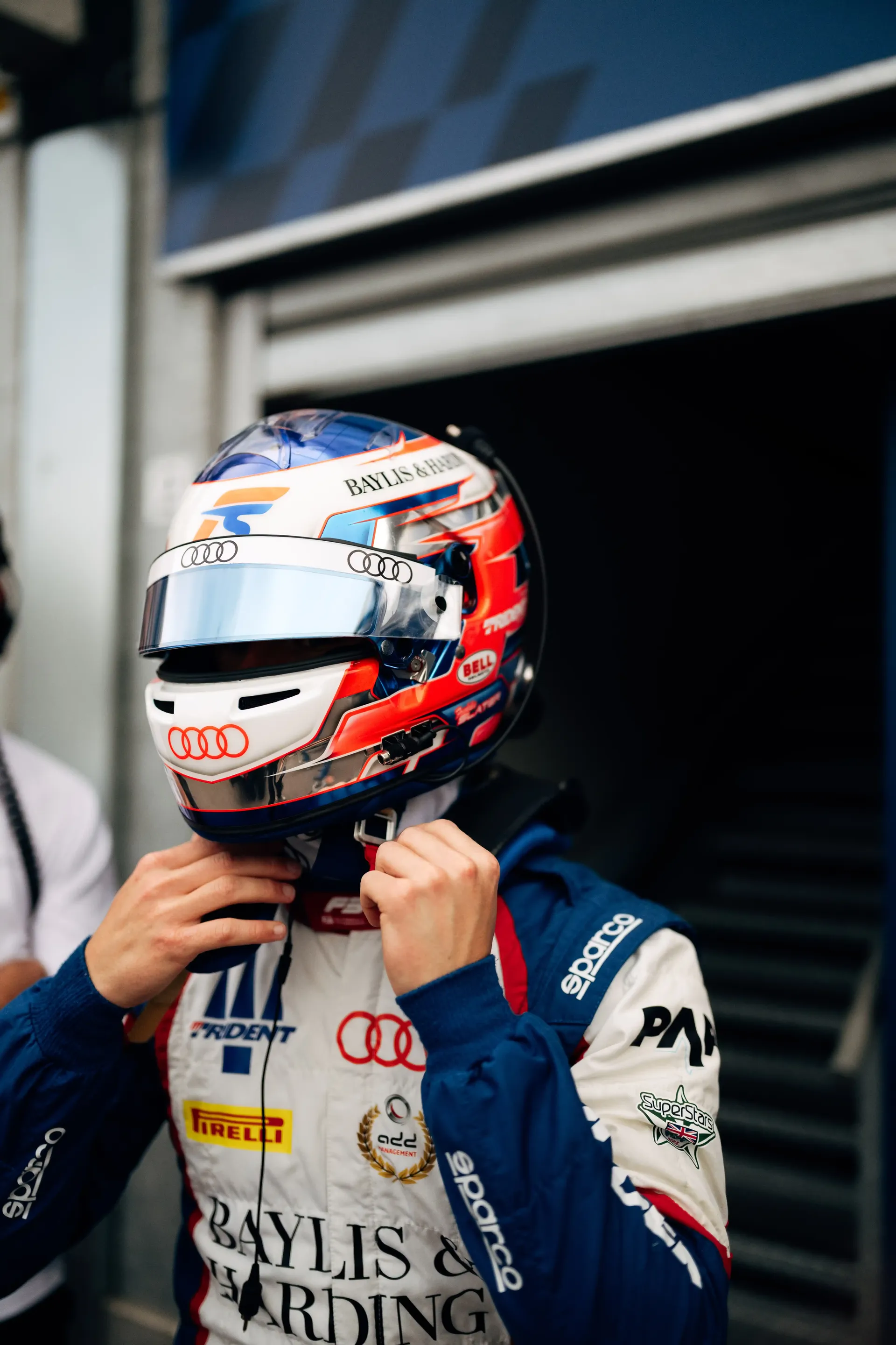 Freddie Slater adjusts the chin strap of his racing helmet while standing outside the Formula 3 garage ahead of a Monaco track session.