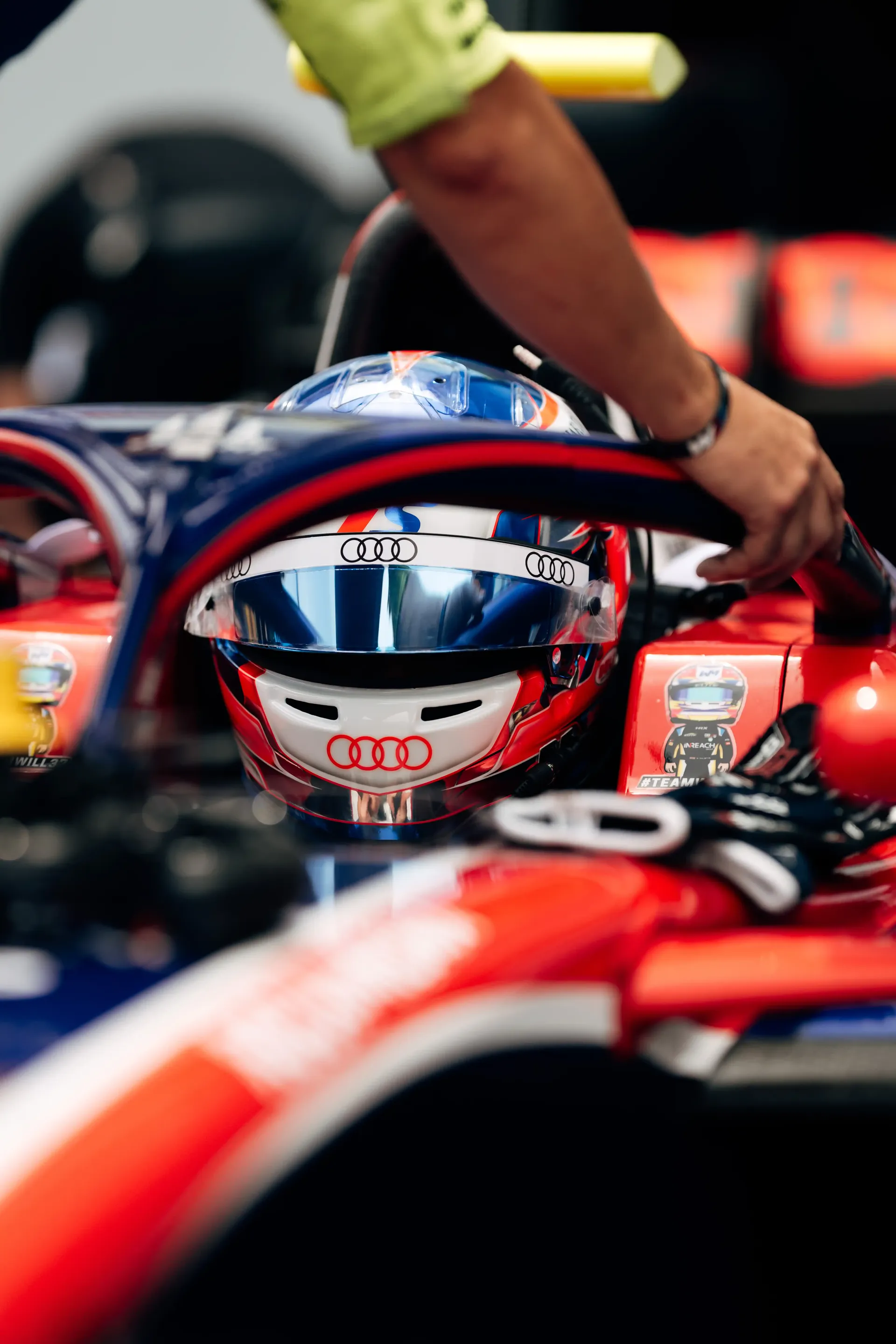 Close-up of Freddie Slater's helmet resting on the cockpit of his FIA Formula 3 car as a mechanic works nearby in the paddock.