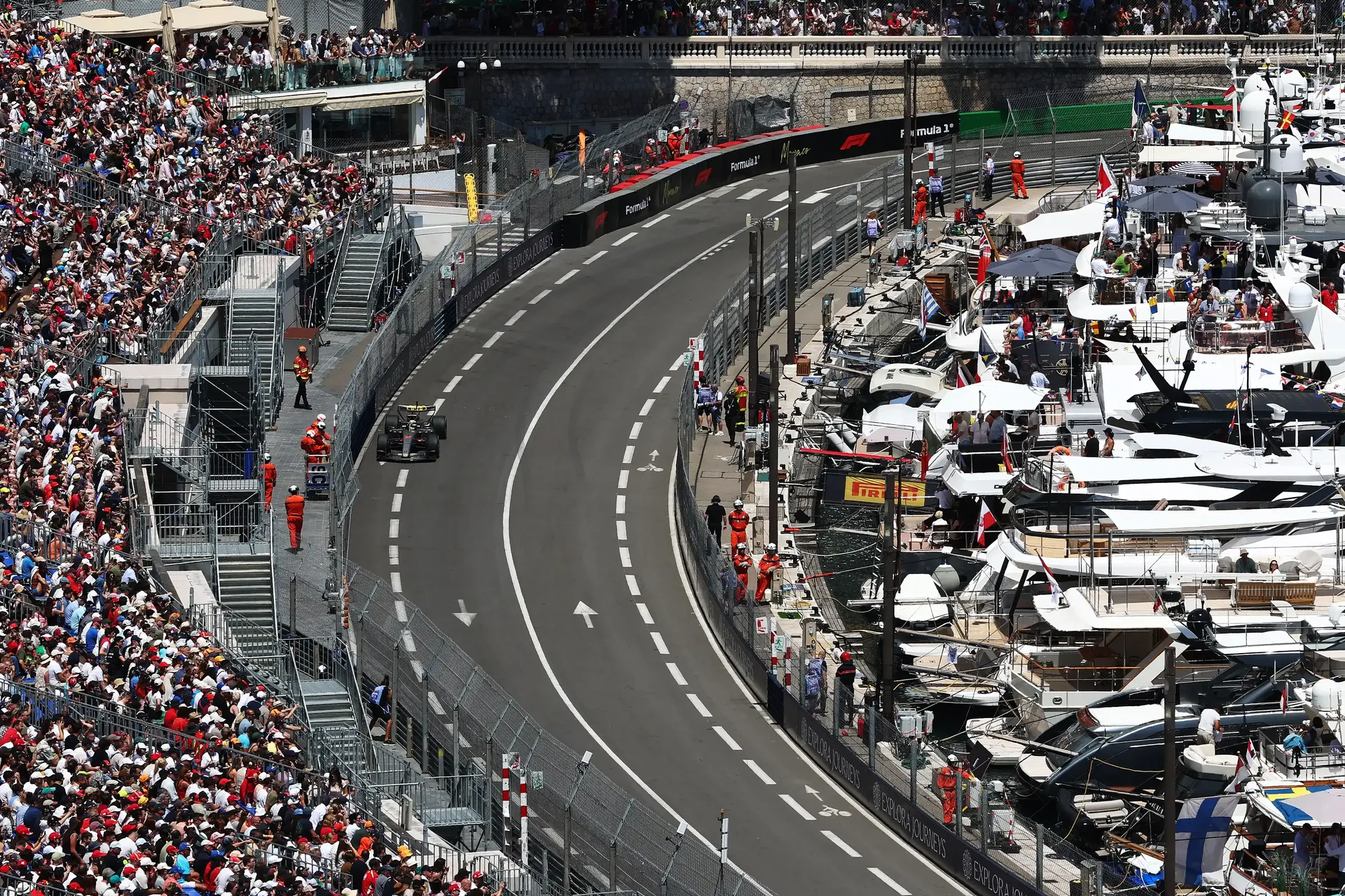 Audi Revolut F1® Team car R26 drives through a sweeping section of the Monaco street circuit during Monaco Grand Prix FP1, with grandstands and the marina visible in the background.
