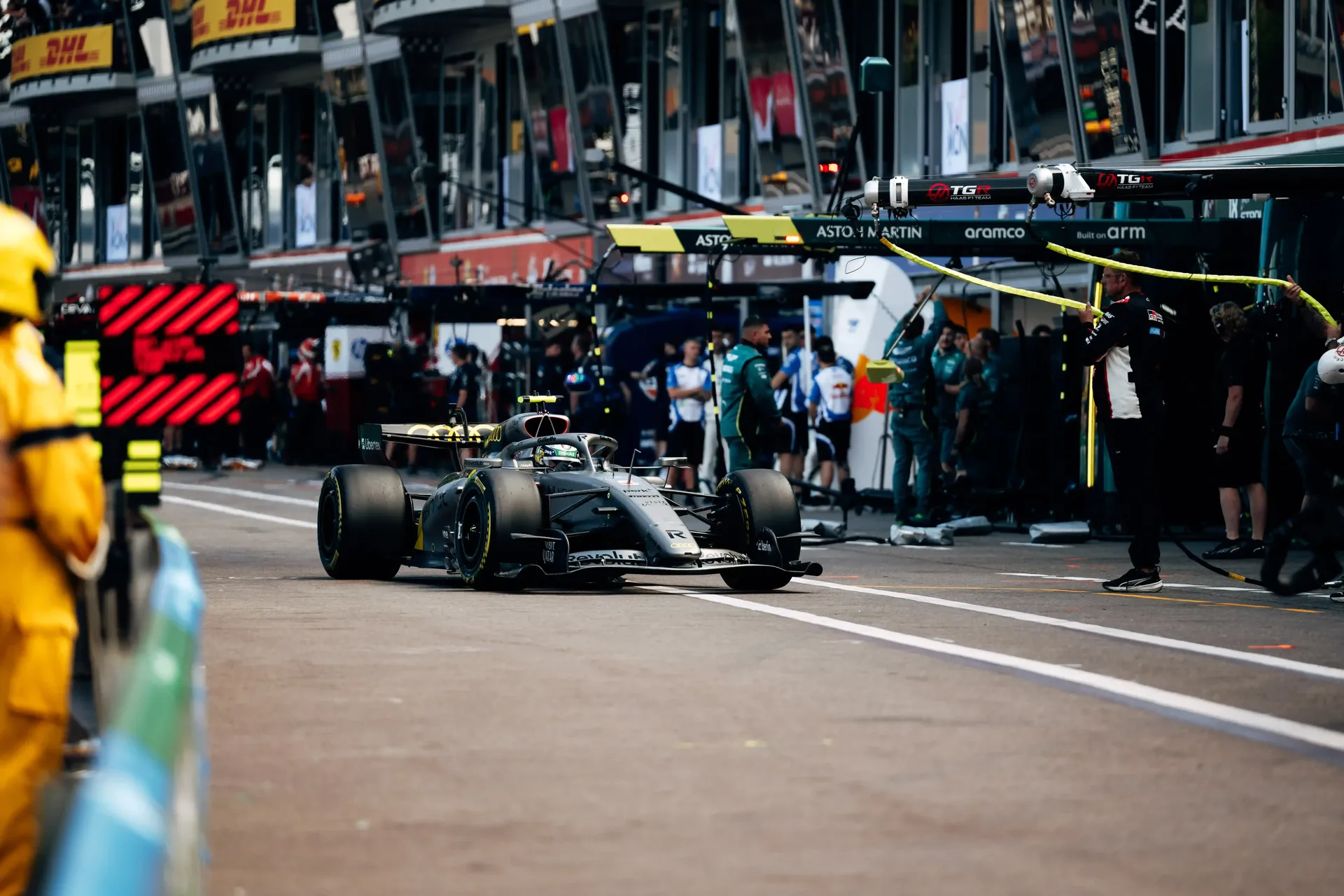 Audi Revolut F1® Team Formula 1 car driving down the pit lane past busy garages.
