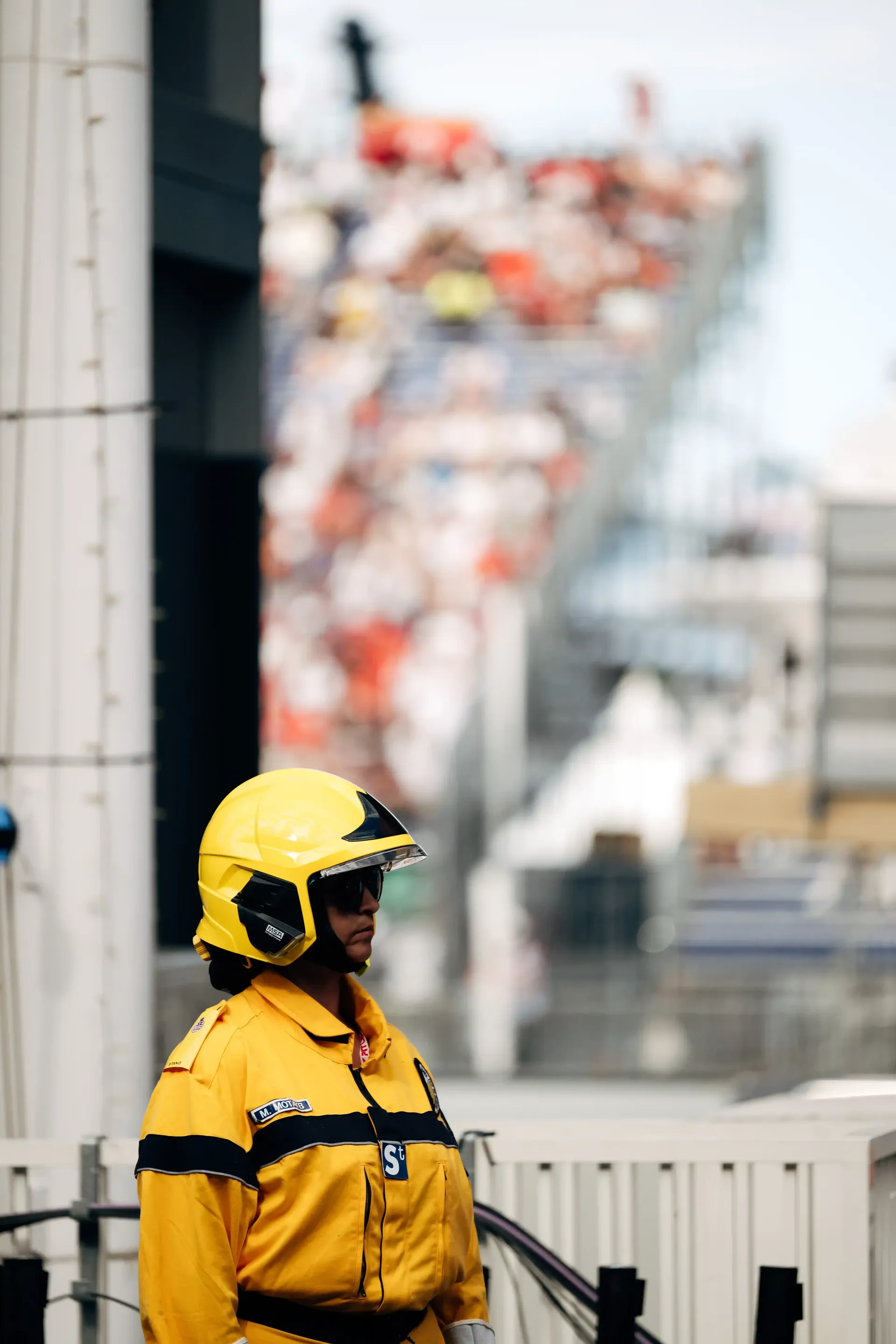 Track marshal in yellow safety gear standing beside a circuit barrier.