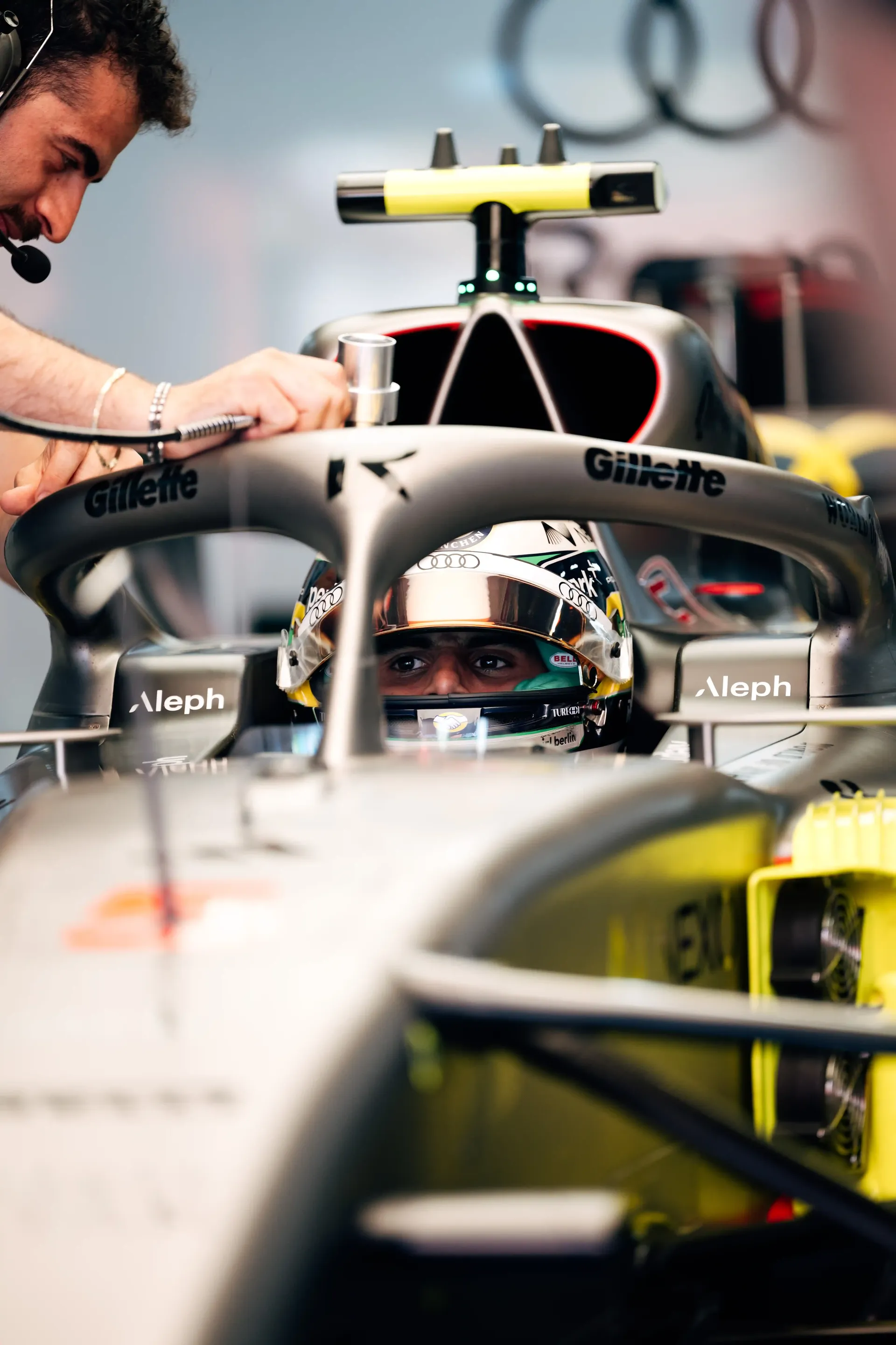 Gabriel Bortoleto visible through the cockpit as a mechanic leans over the Audi Revolut F1® Team car R26 in the garage.